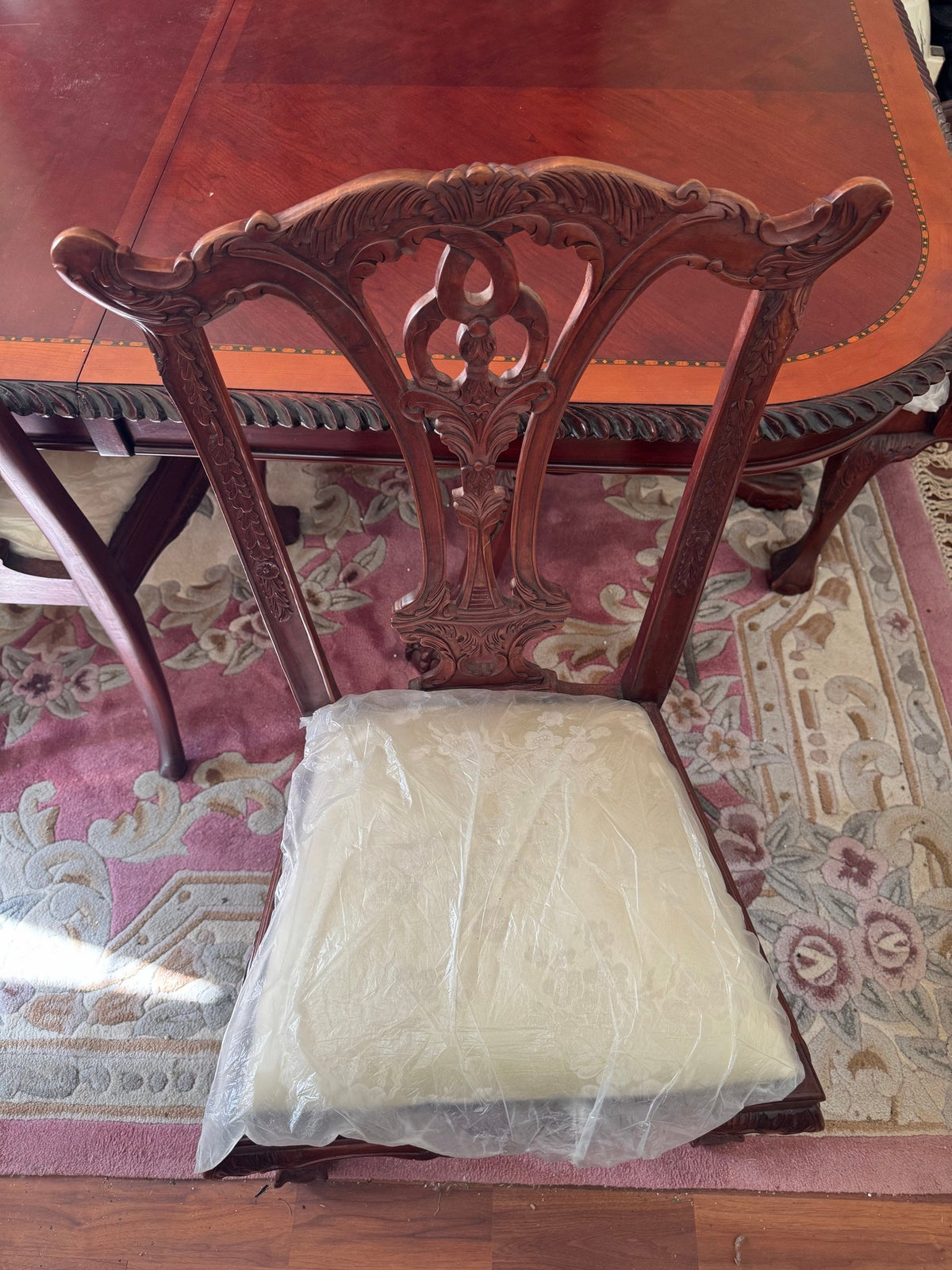Side chair with carved splat back and plastic-wrapped seat beside the table