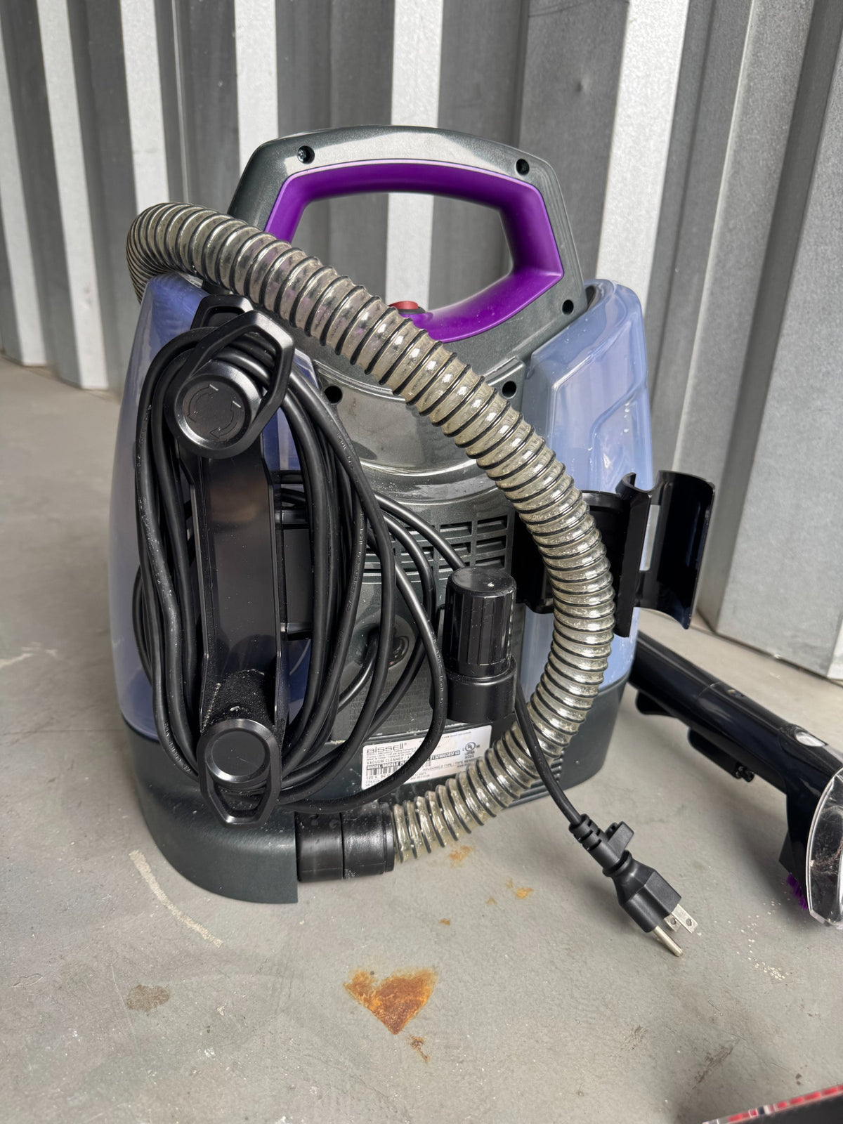 Portable carpet cleaner unit from rear angle showing purple handle, coiled hose, and power cord arrangement