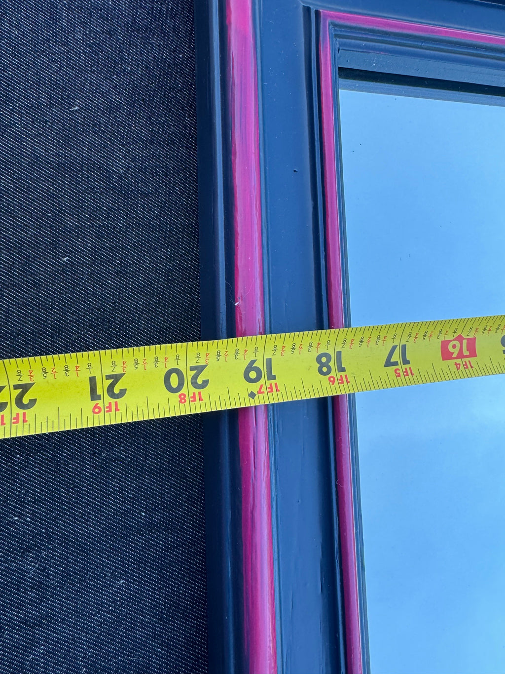 Close-up of tape measure showing width measurement of approximately 16 inches across pink and navy framed mirror