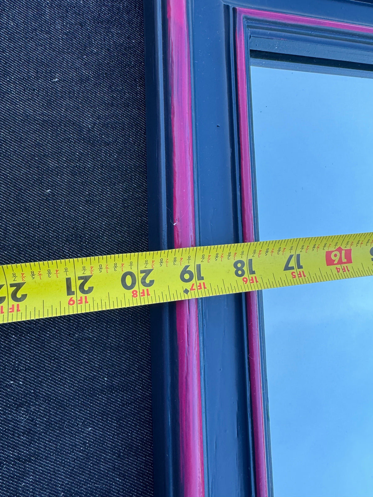 Close-up of tape measure showing width measurement of approximately 16 inches across pink and navy framed mirror
