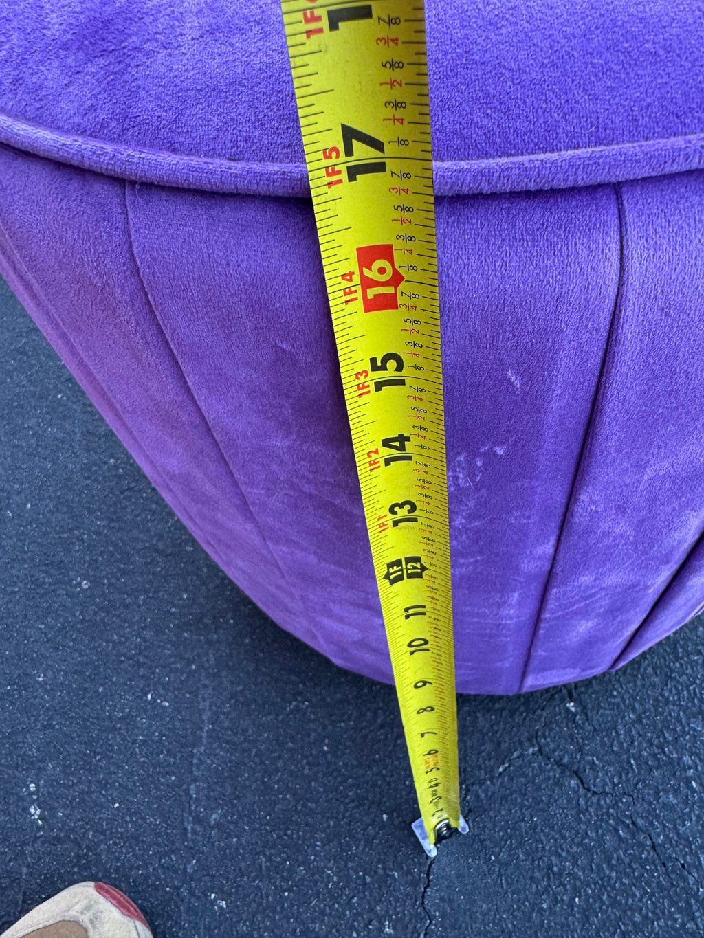 Close-up of purple velvet ottoman top measuring approximately 15 inches diameter with tape measure