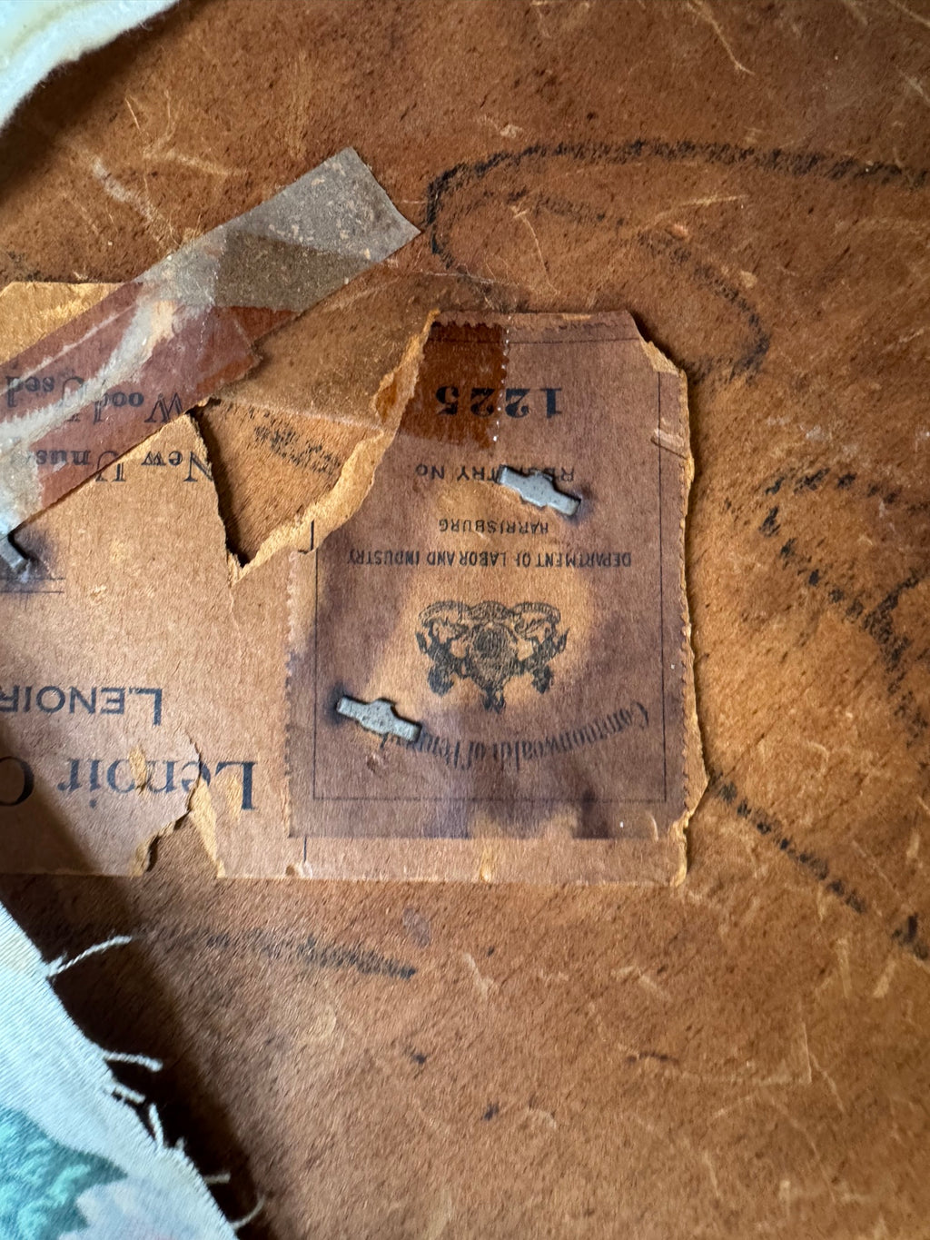 Close-up of deteriorated leather furniture label with worn text and decorative emblem visible