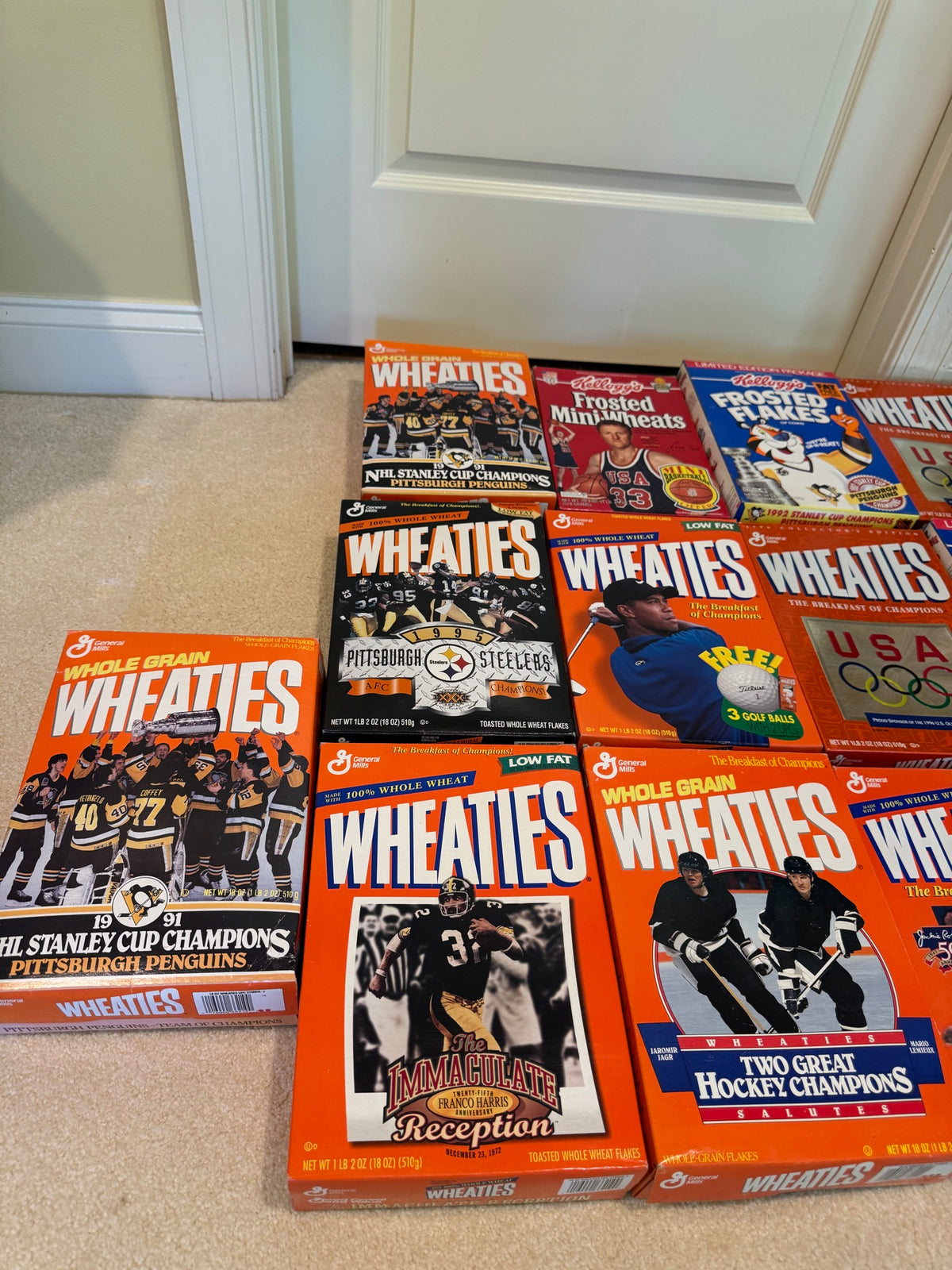 Close-up view of cereal boxes arranged on carpet, featuring Wheaties and Frosted Flakes boxes with Pittsburgh Penguins, Steelers, and Olympics branding