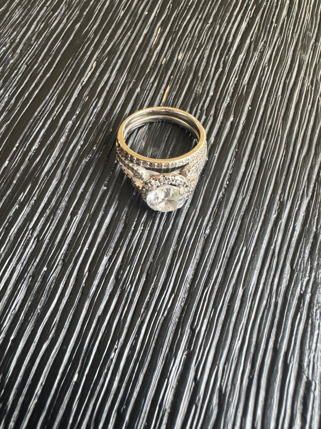 Diamond halo ring with pave shoulders displayed on textured dark surface, top-down view