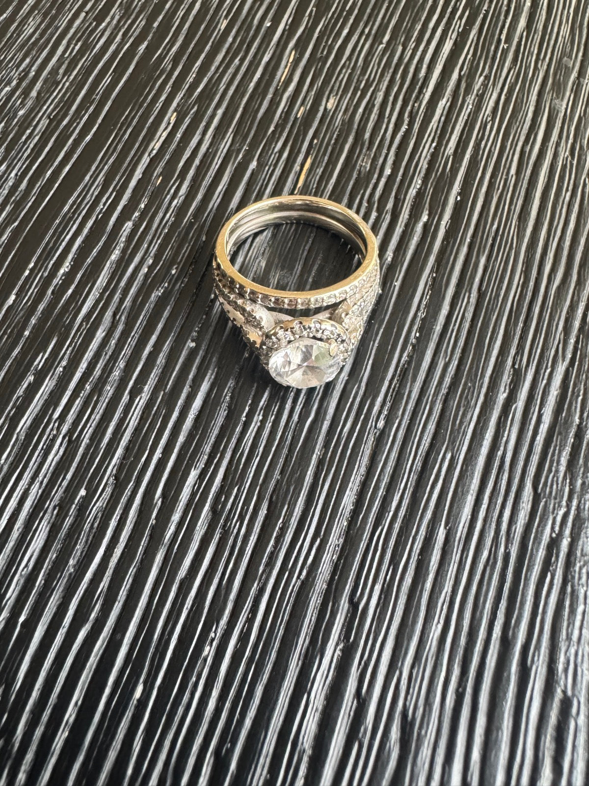 Diamond halo ring with pave shoulders displayed on textured dark surface, top-down view