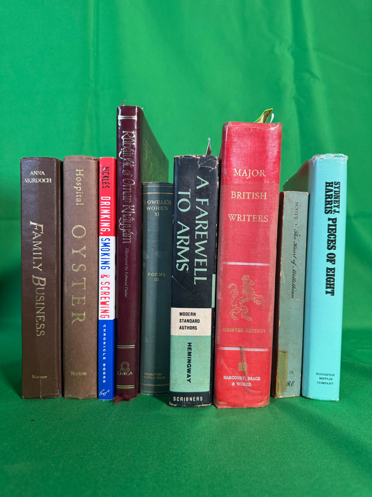 Books stood spine-out on green cloth, including the Rubáiyát of Omar Khayyám illustrated by Edmund Dulac, A Farewell to Arms by Ernest Hemingway, Major British Writers and Lowell's Works Volume XI