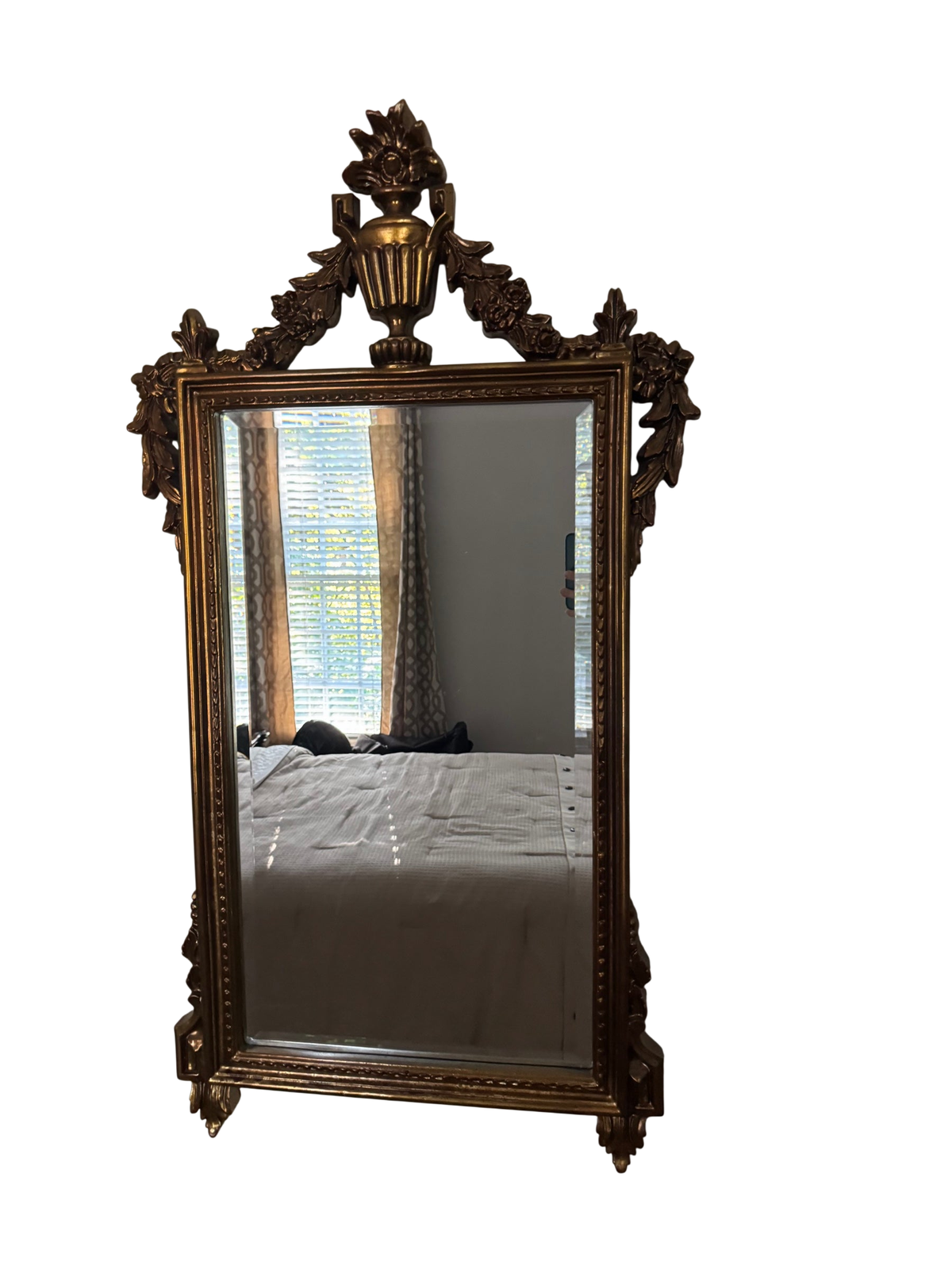 Tall gold gilt wall mirror with an ornate carved urn and floral crest, hanging on a gray wall