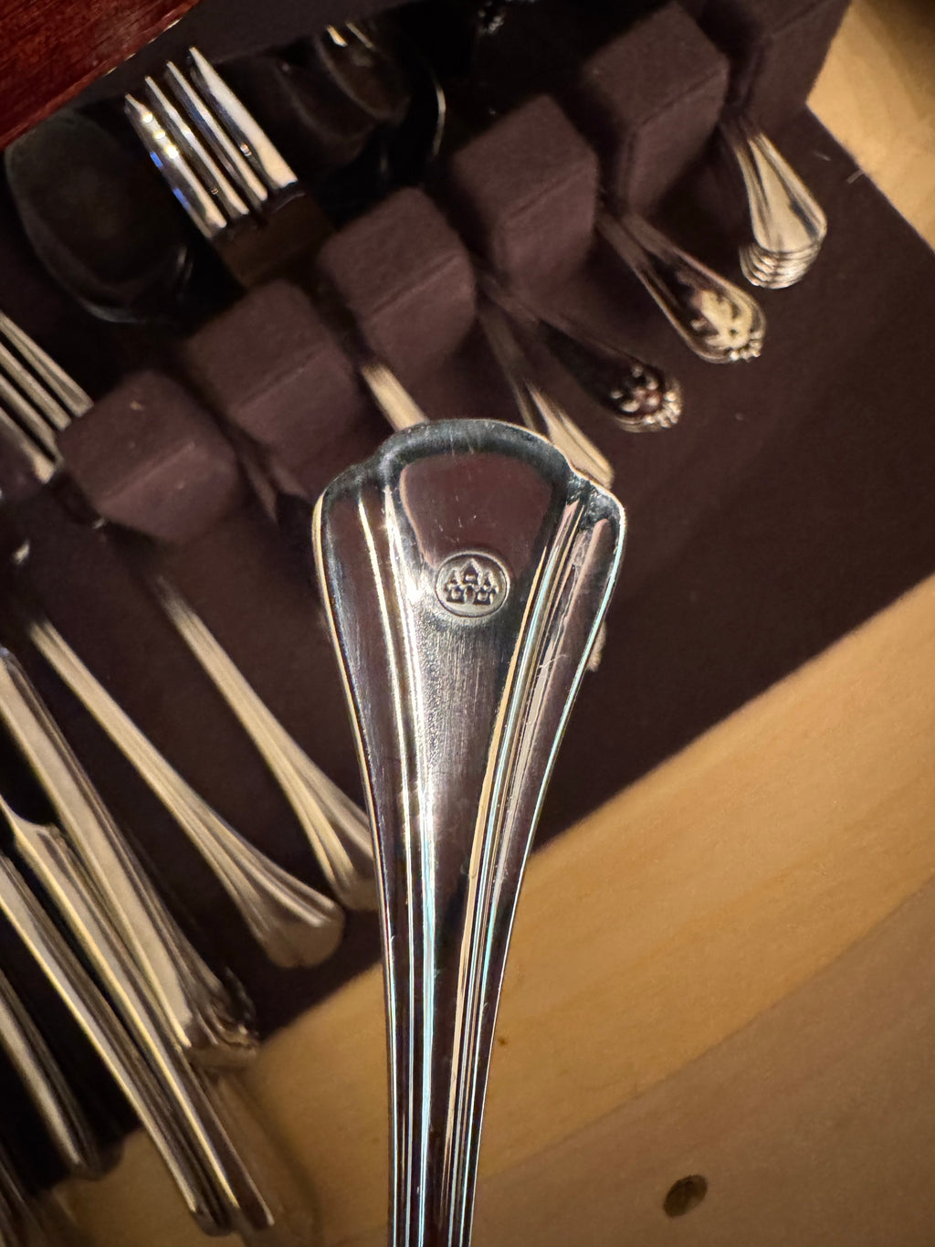Close-up of a fork handle showing a small oval maker's stamp on reeded pattern flatware