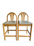 Pair of natural wood bar stools with curved backrest, woven rush seats, and turned legs from front view