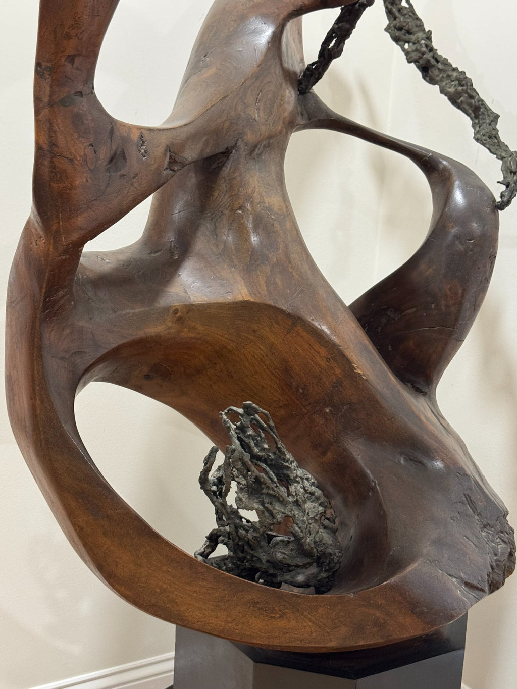 Close-up of dark textured accent material embedded in lower carved section, showing rough contrast against smooth wood surface