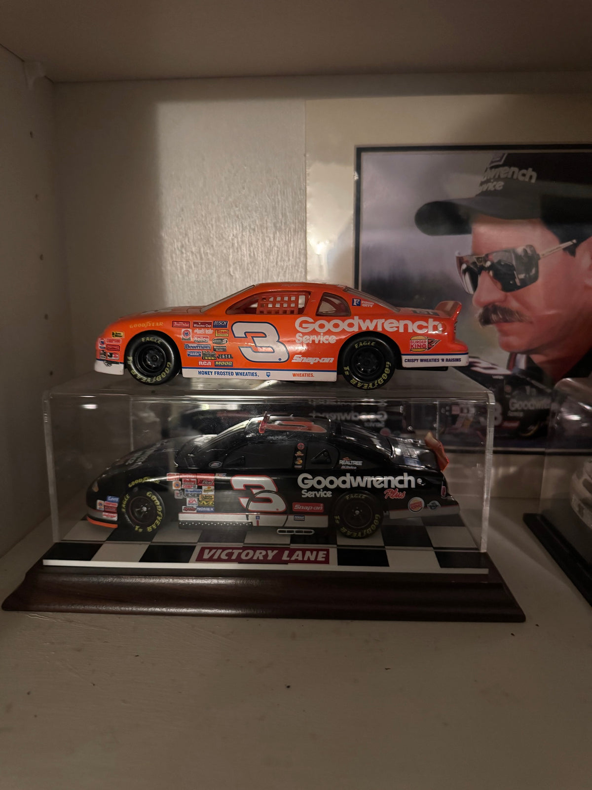 Orange Wheaties Goodwrench #3 car above the black Goodwrench Plus #3 car in a Victory Lane display case