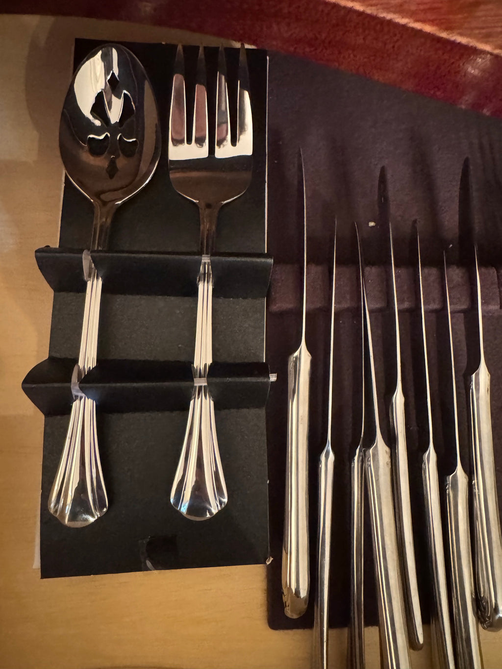 Serving spoon and fork with pierced and solid bowls next to a row of dinner knives