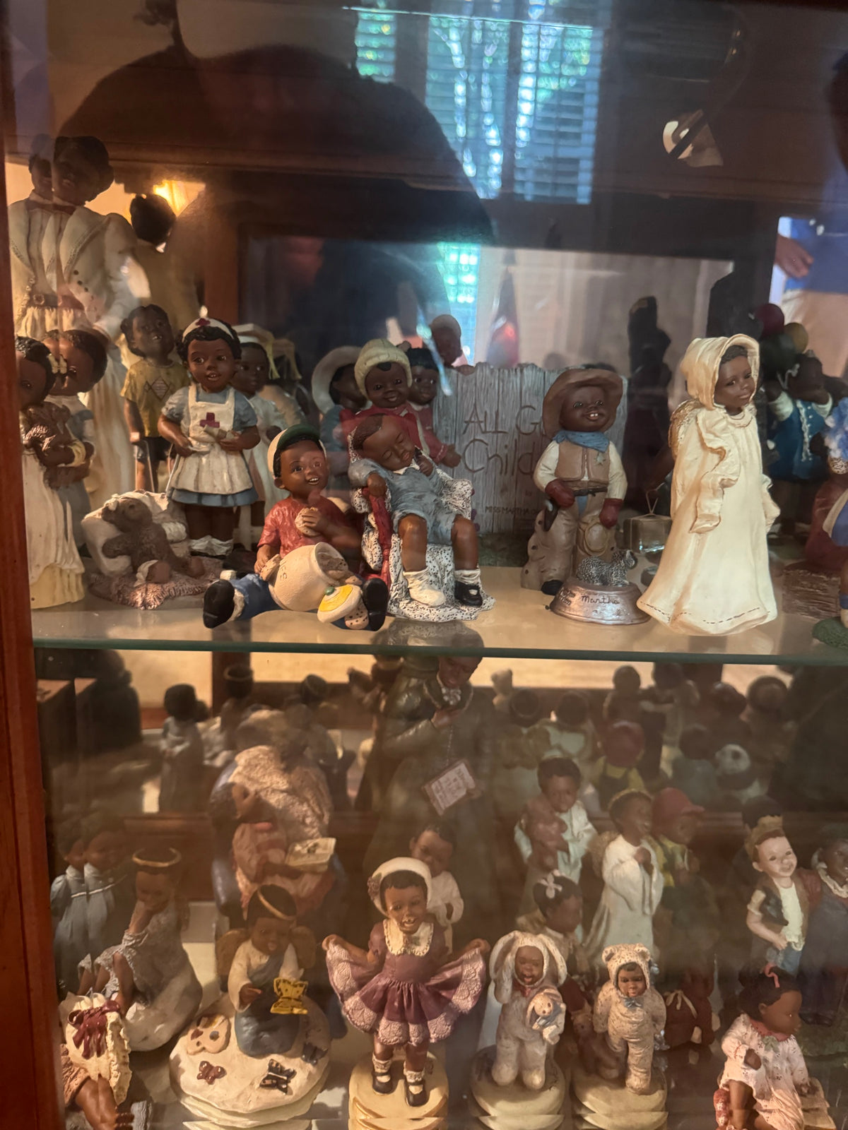 Shelf of All God's Children figurines with a boy and girl seated together, a cowboy figure, and an angel figurine near a wood fence sign