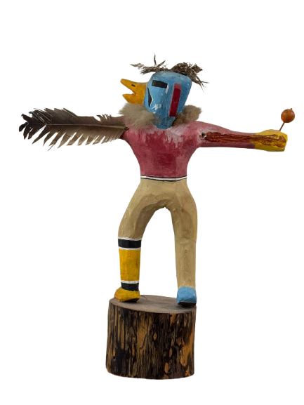 Full frontal view of carved wooden kachina figure with outstretched arms, feathered wings, painted blue head and red torso on wooden base