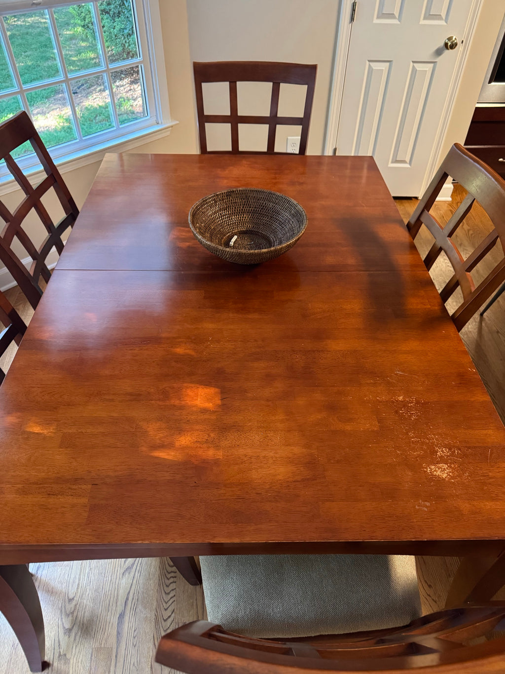 Overhead view of cherry dining table top showing surface scratches and a woven wood bowl