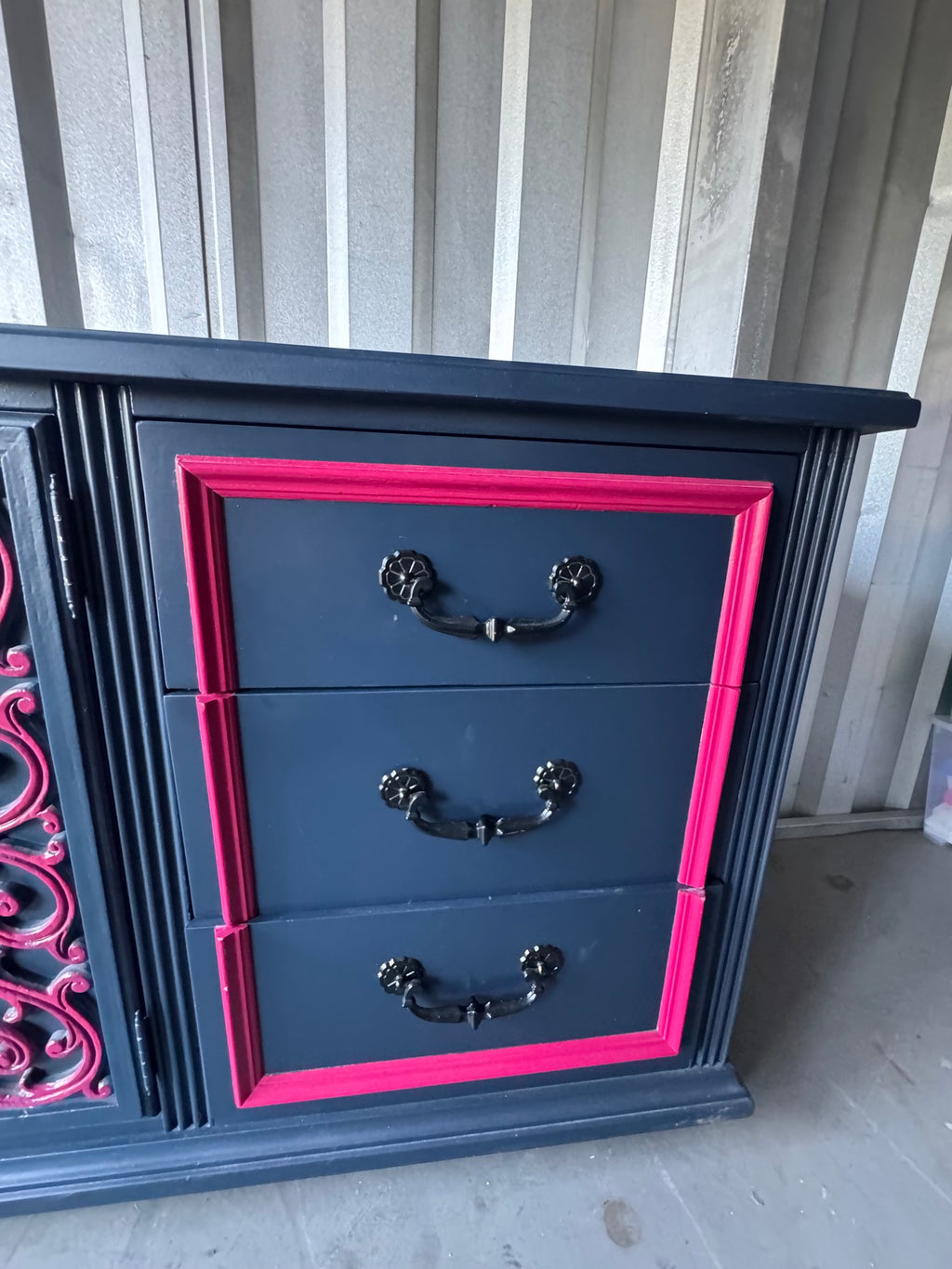 Navy dresser with three drawers, pink frame trim, and black handles, front view on concrete