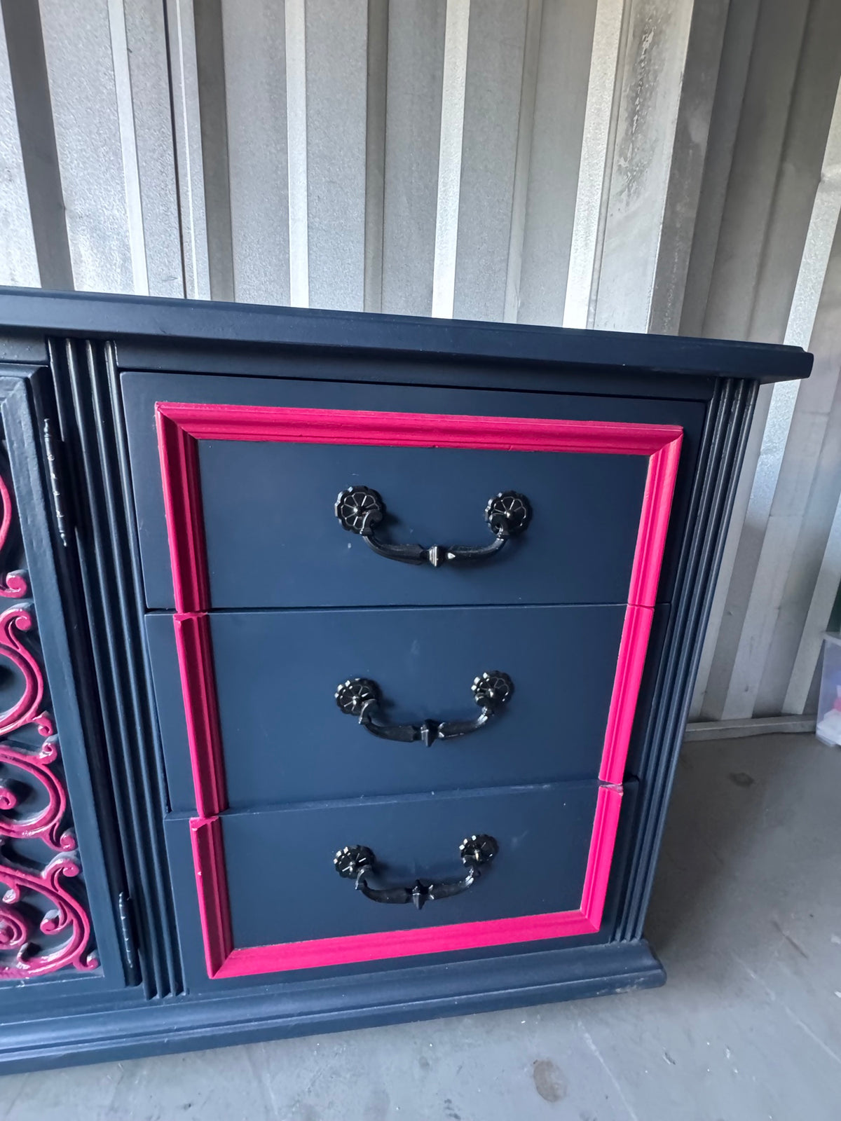 Navy dresser with three drawers, pink frame trim, and black handles, front view on concrete