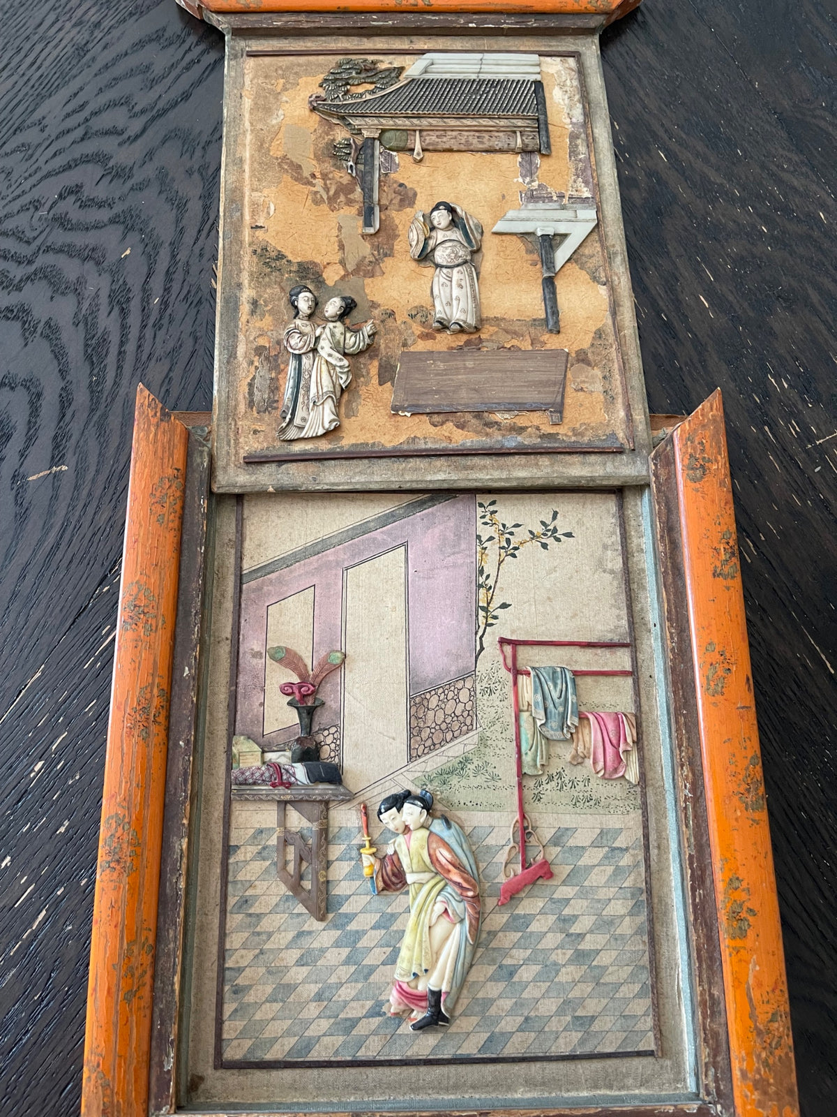 Two-panel wooden frame showing upper relief carving scene with pagoda and figures, lower hand-painted interior courtyard scene with figures and furnishings