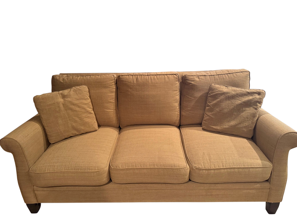 Tan upholstered three-cushion sofa with rolled arms, decorative pillows, and dark espresso wooden feet, front view
