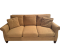 Tan upholstered three-cushion sofa with rolled arms, decorative pillows, and dark espresso wooden feet, front view