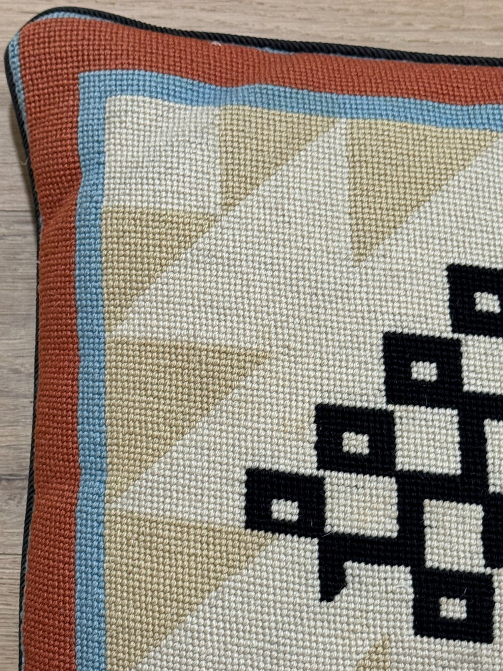 Close-up of pillow corner showing rust border, blue trim, and black and white geometric design detail