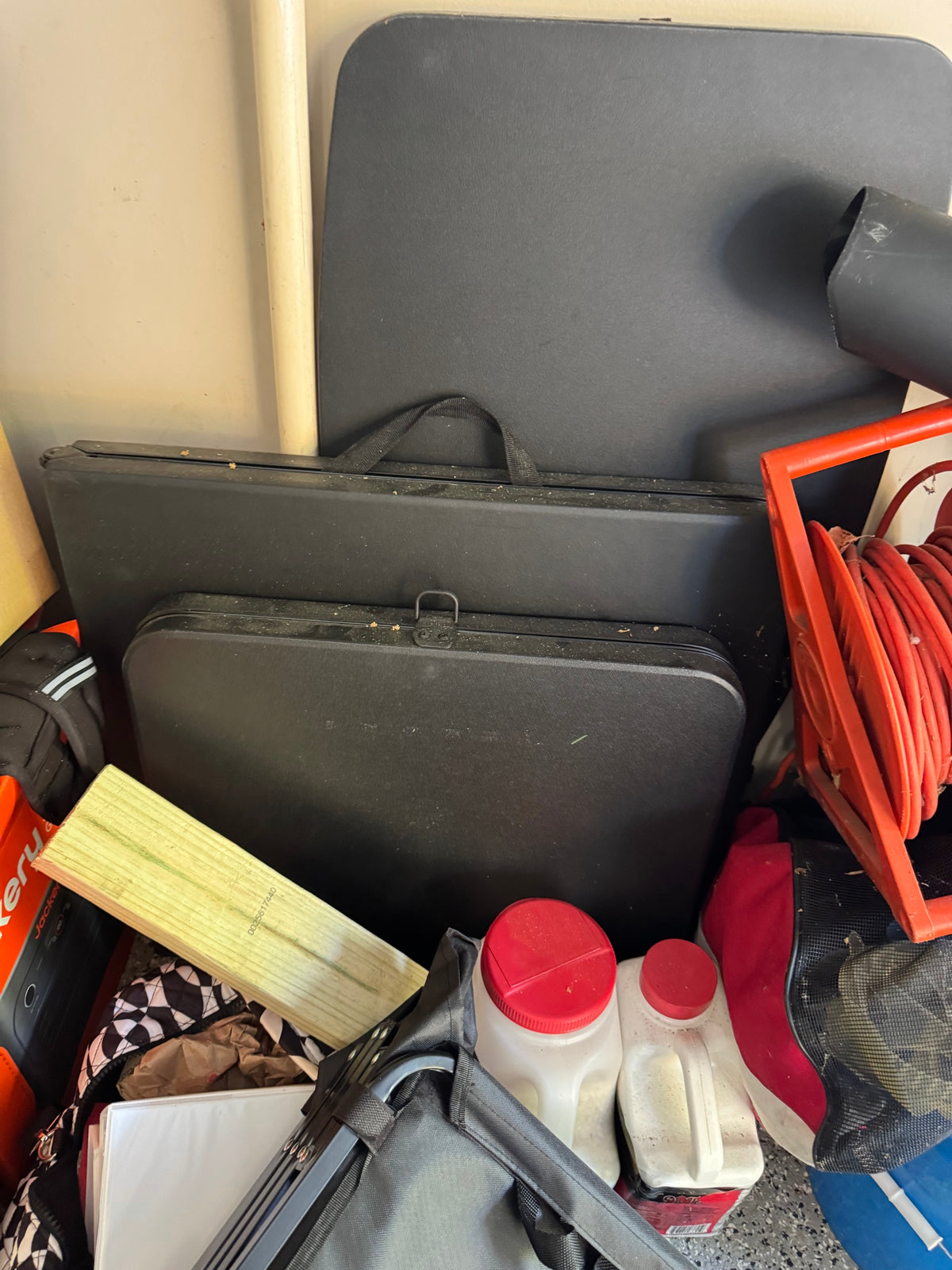 Garage lot of black folding tables, an orange extension cord reel, a wood plank, plastic jugs, and a bag