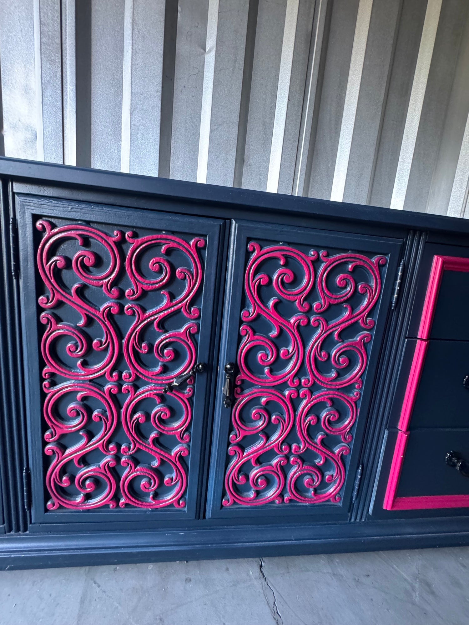 Cabinet doors with elaborate pink scrollwork filigree pattern on navy background, frontal view