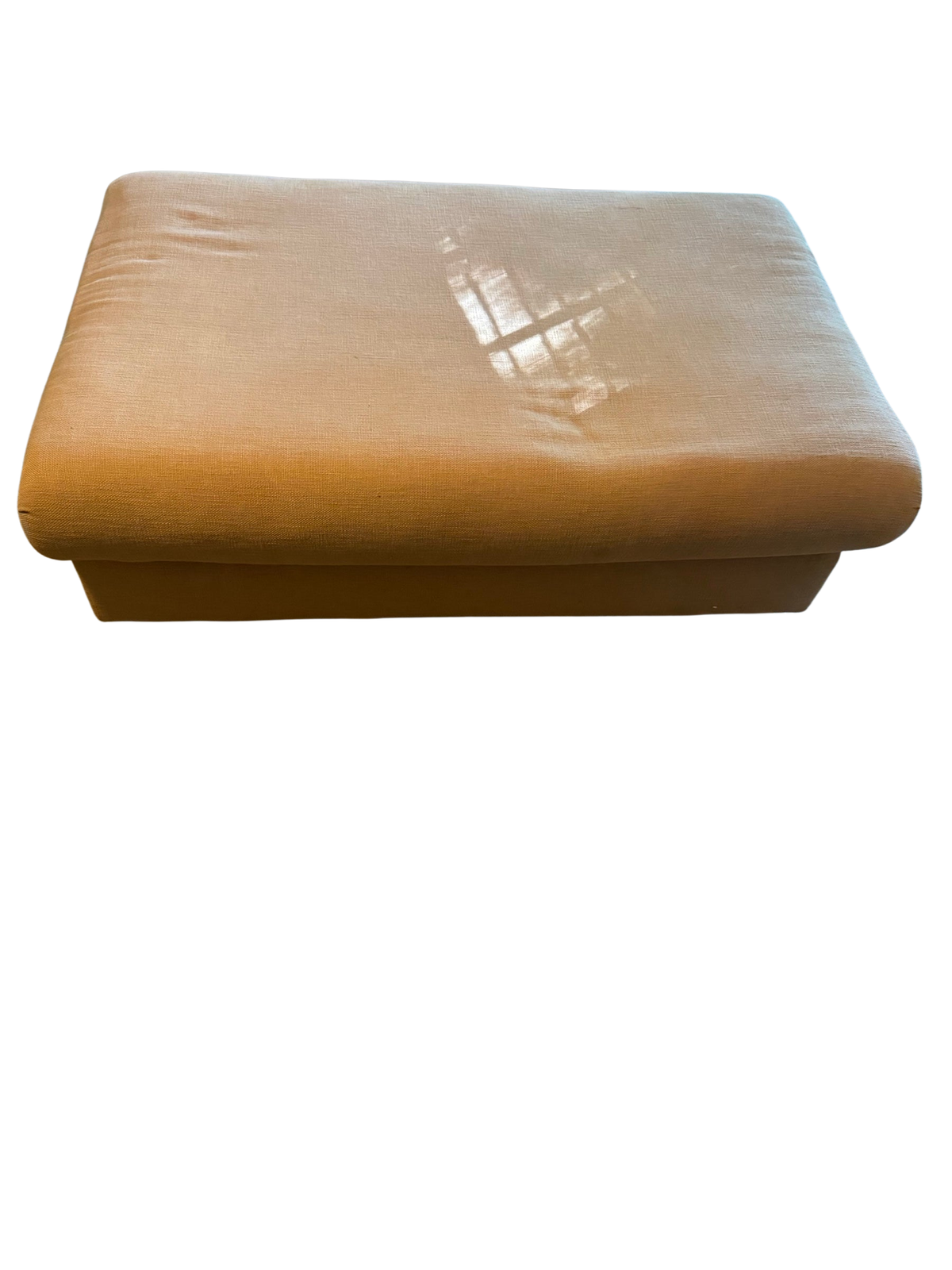 Tan linen storage ottoman with lift-top lid on carpeted floor in front of a sofa