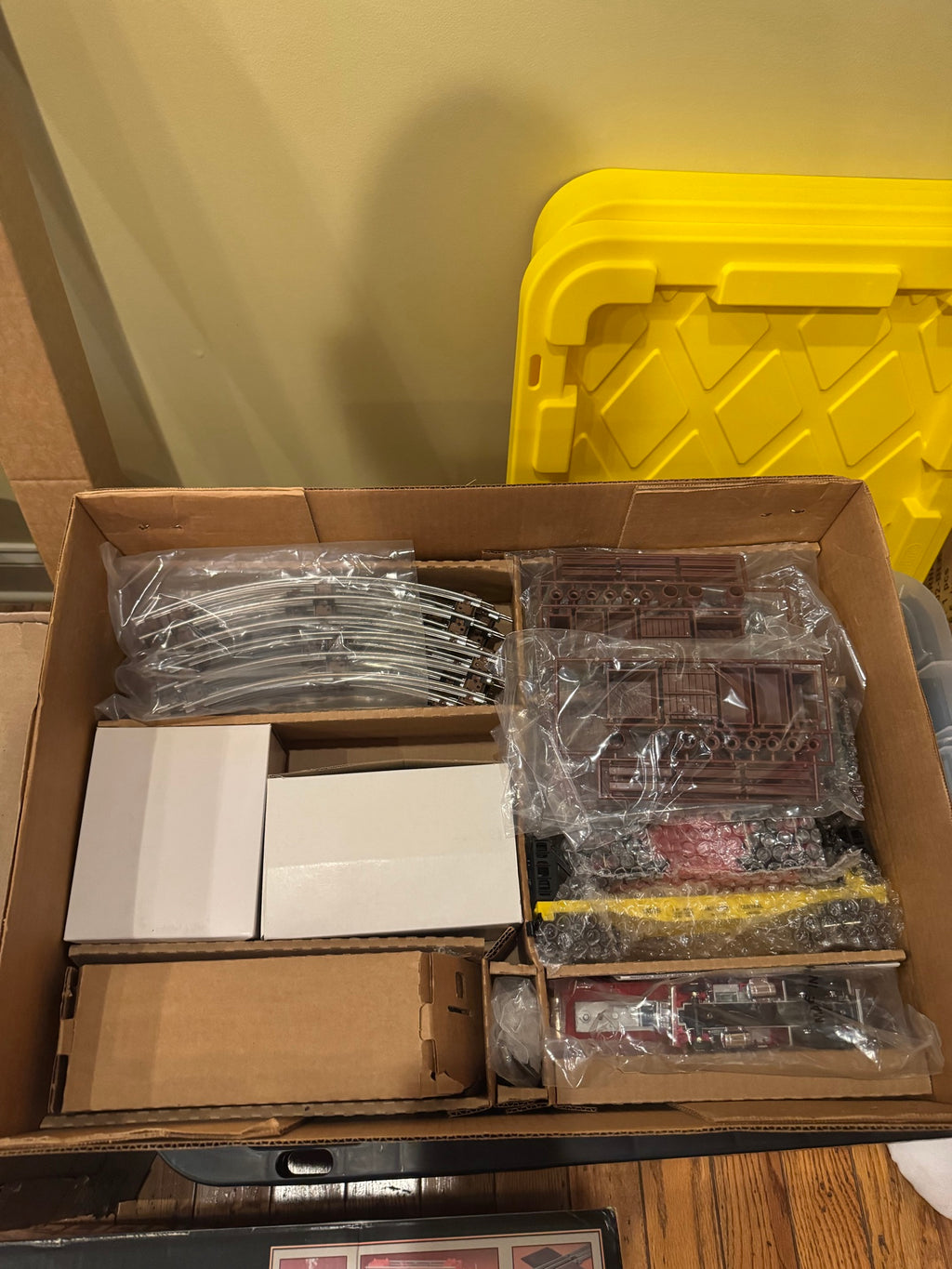Interior of opened box revealing track sections in plastic bags, instruction manuals, and various train car components wrapped in plastic