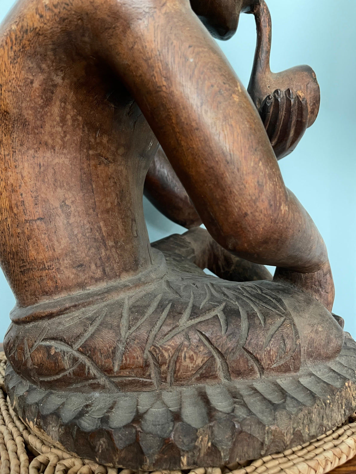 Detail of figure's lap area showing carved loincloth with geometric patterns and woven base