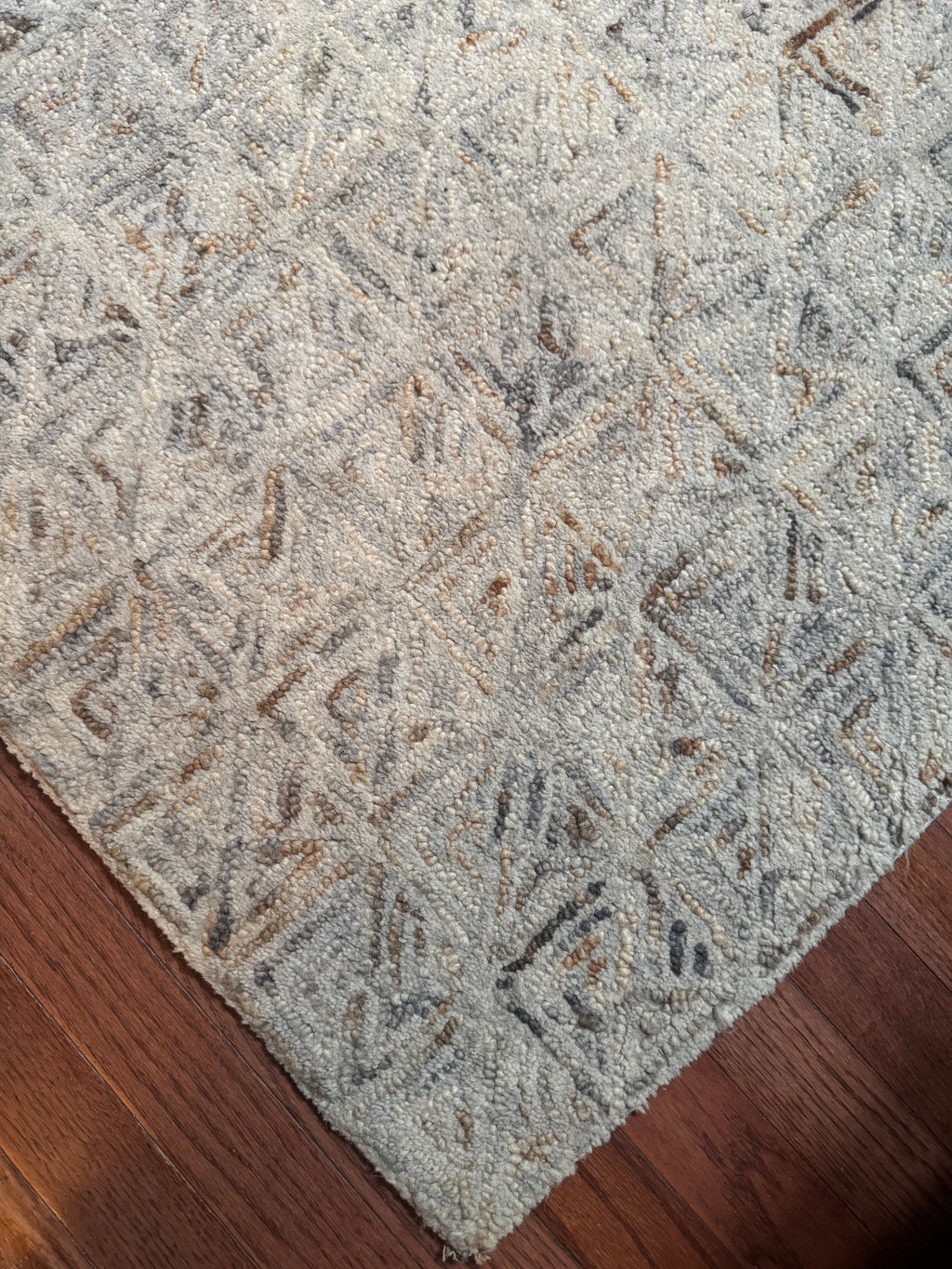 Folded corner of a grey and ivory geometric area rug resting on a hardwood floor