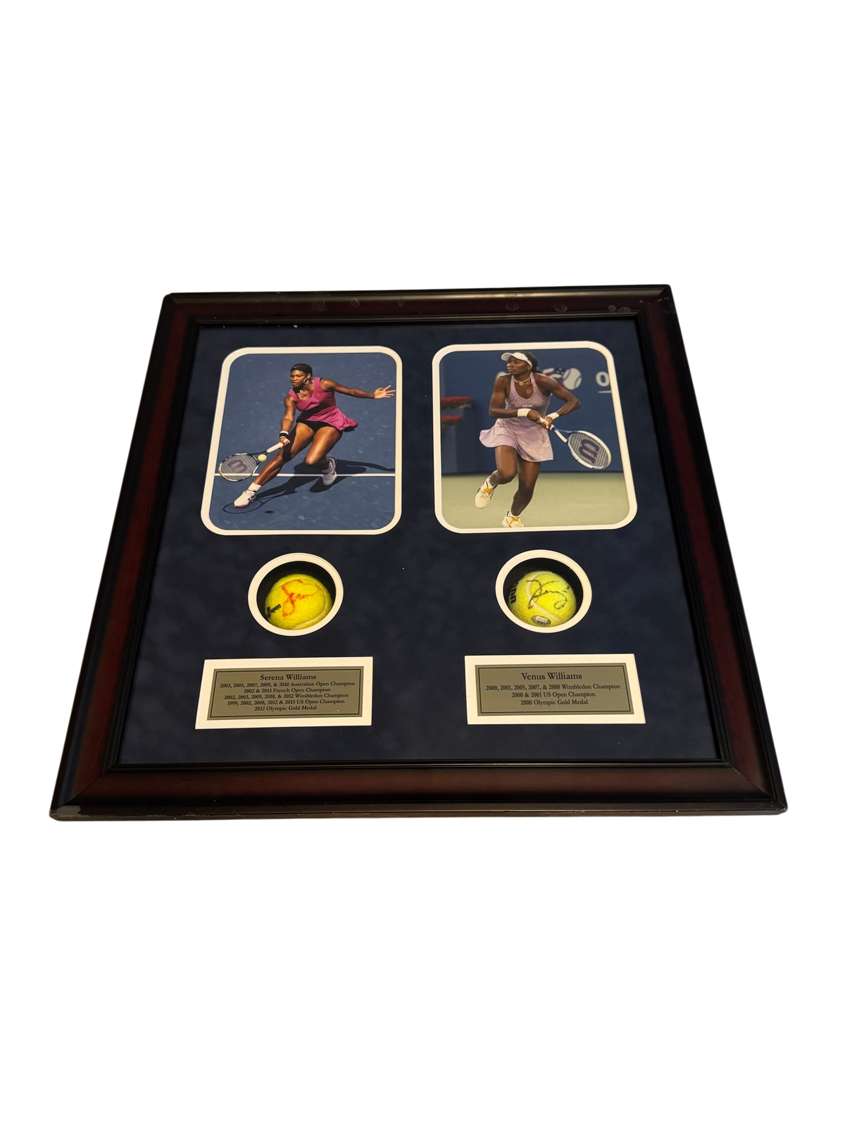 Framed display with photos of Serena and Venus Williams and two signed tennis balls in cutouts, resting on a bed