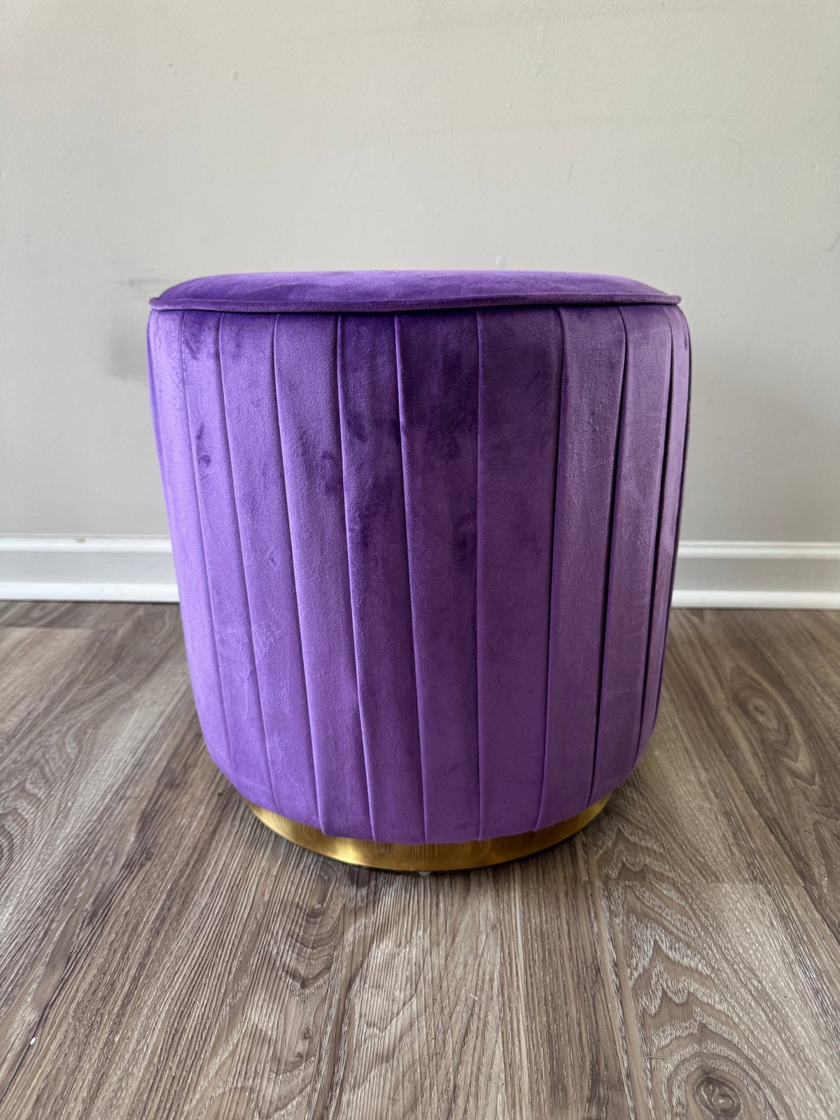 Purple velvet cylindrical ottoman with vertical channel tufting and gold metal base ring, side view