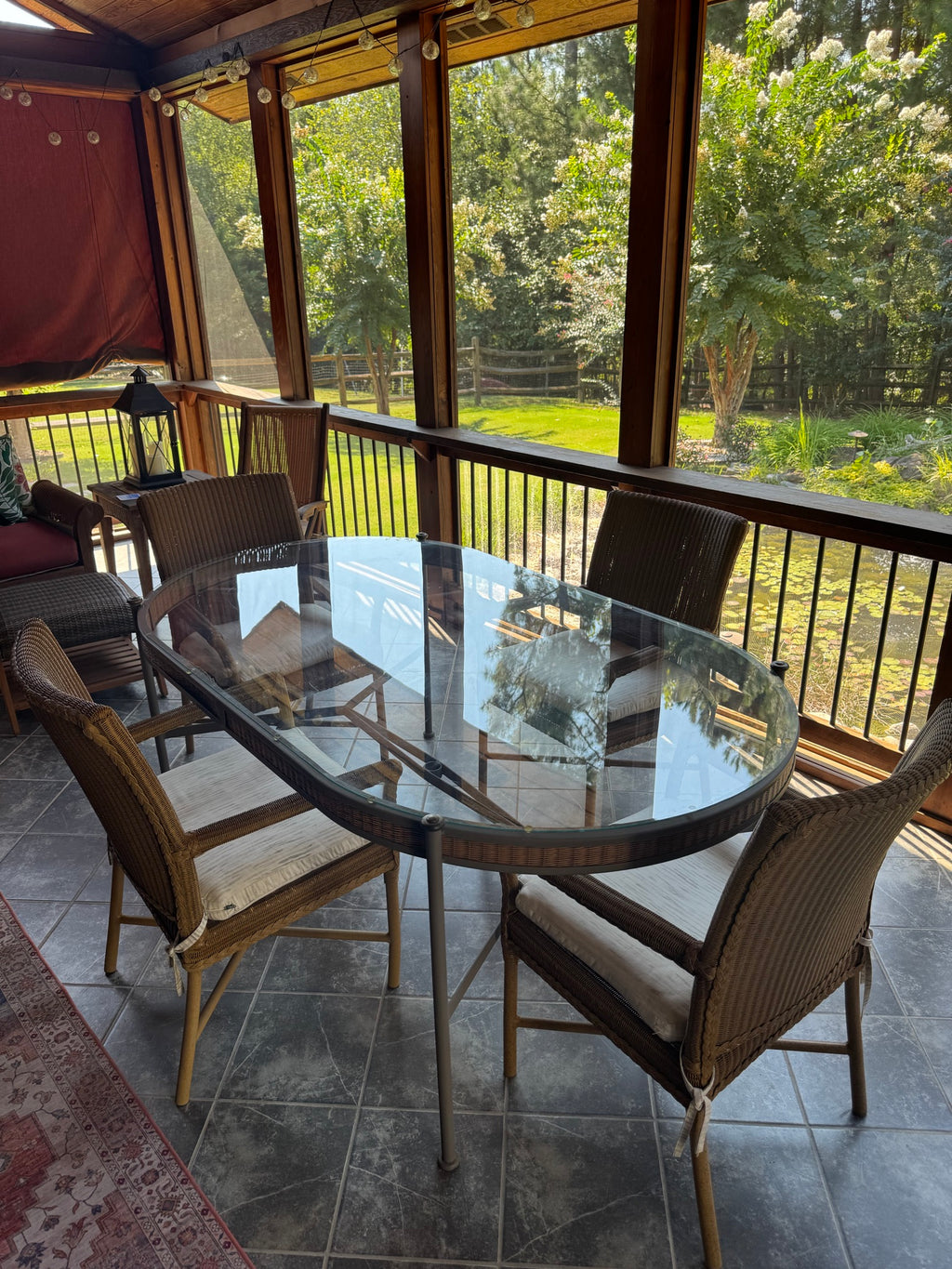 Close-up of oval glass table top reflecting interior and exterior, surrounded by wicker chairs with cushions