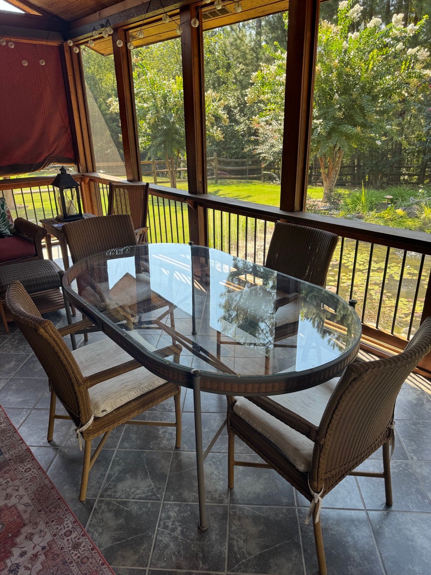 Close-up of oval glass table top reflecting interior and exterior, surrounded by wicker chairs with cushions