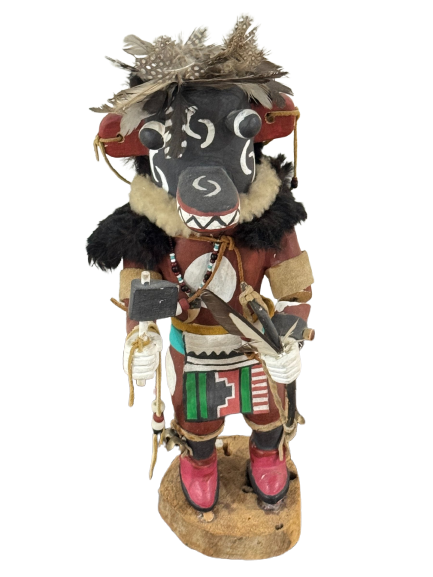 Front view of complete Hopi Kachina doll with black carved head, feathered headdress, fur collar, and painted body on wooden base