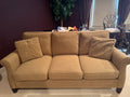 Tan upholstered three-cushion sofa with rolled arms, decorative pillows, and dark espresso wooden feet, front view