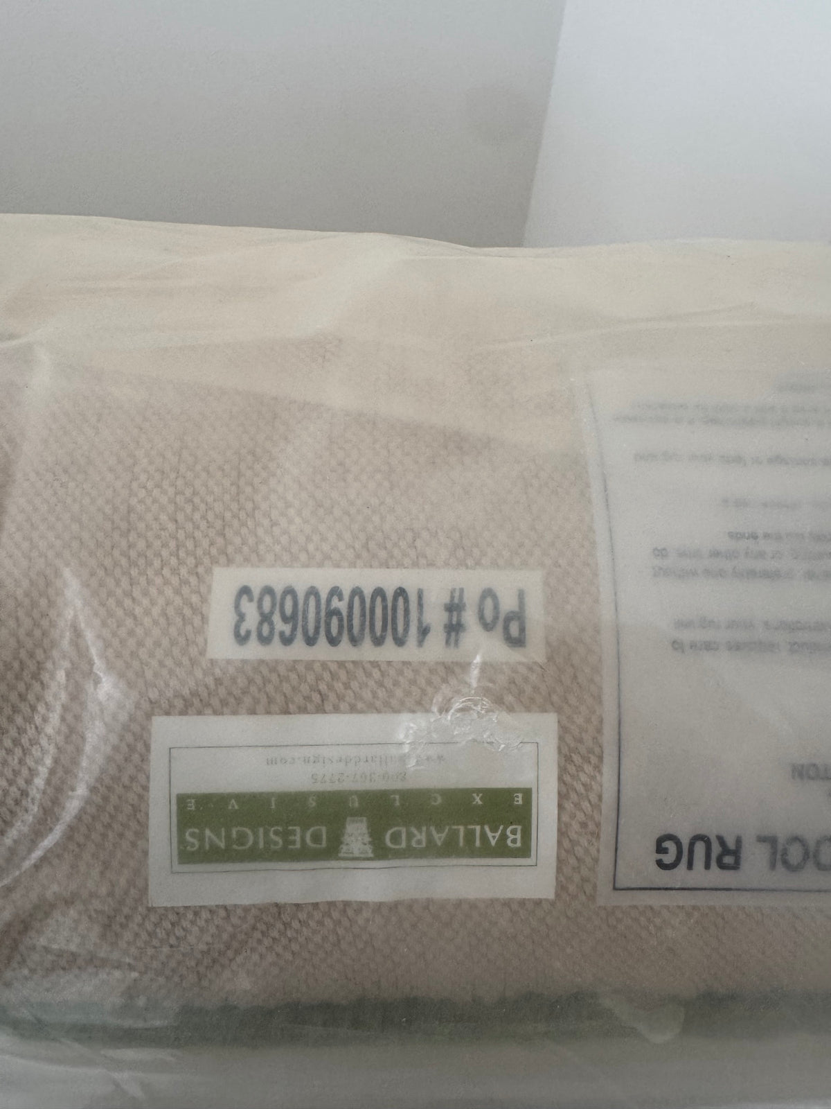 Ballard Designs label on cream wool rug showing product number 10060008L, folded corner visible