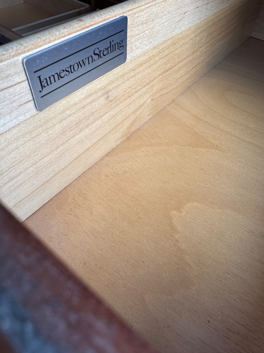 Close-up of Jamestown Sterling maker's label on light wood surface, black text on silver metallic background