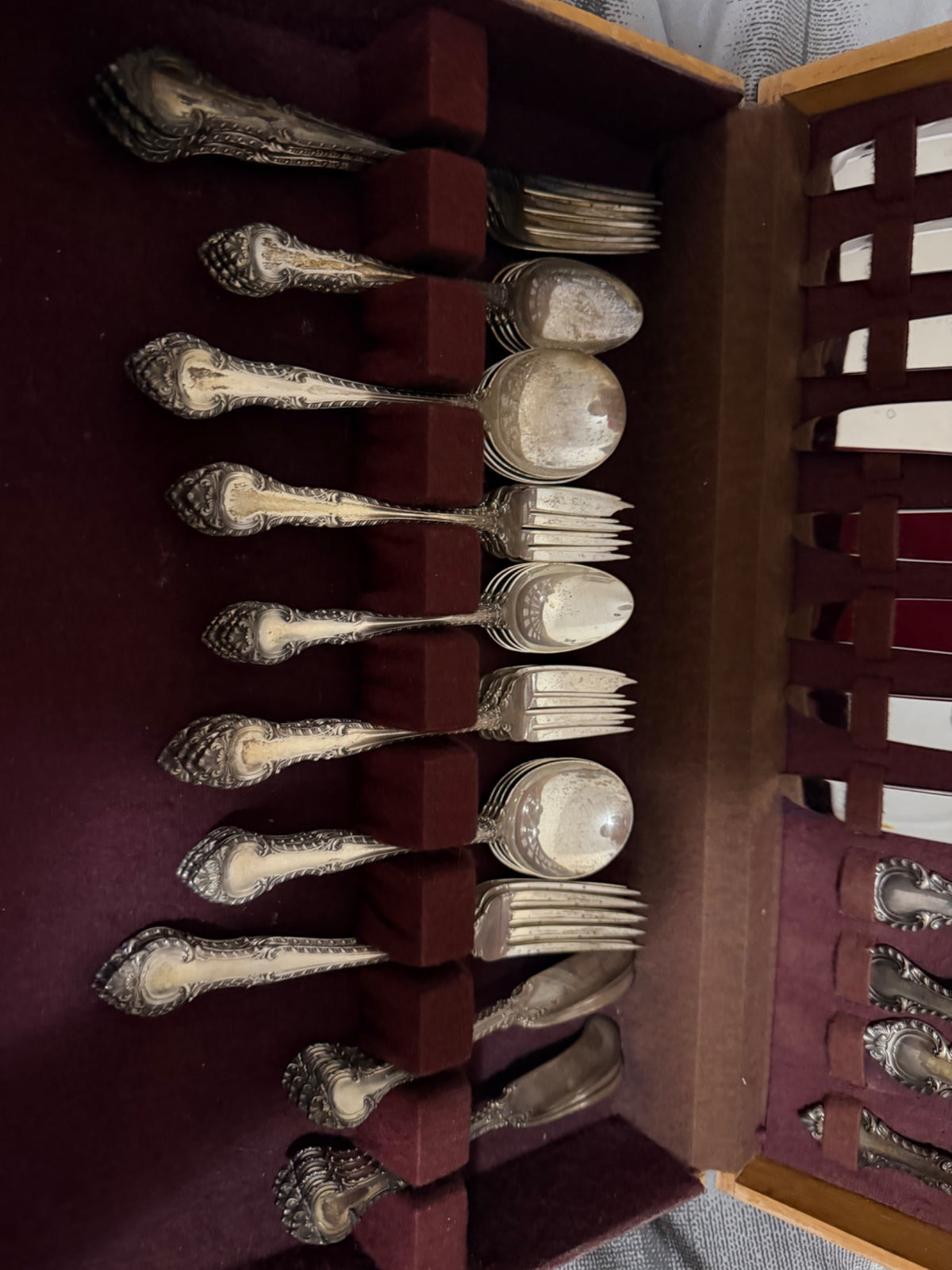 Lower drawer of chest open showing additional flatware pieces stacked in sections with ornate handles and polished bowls