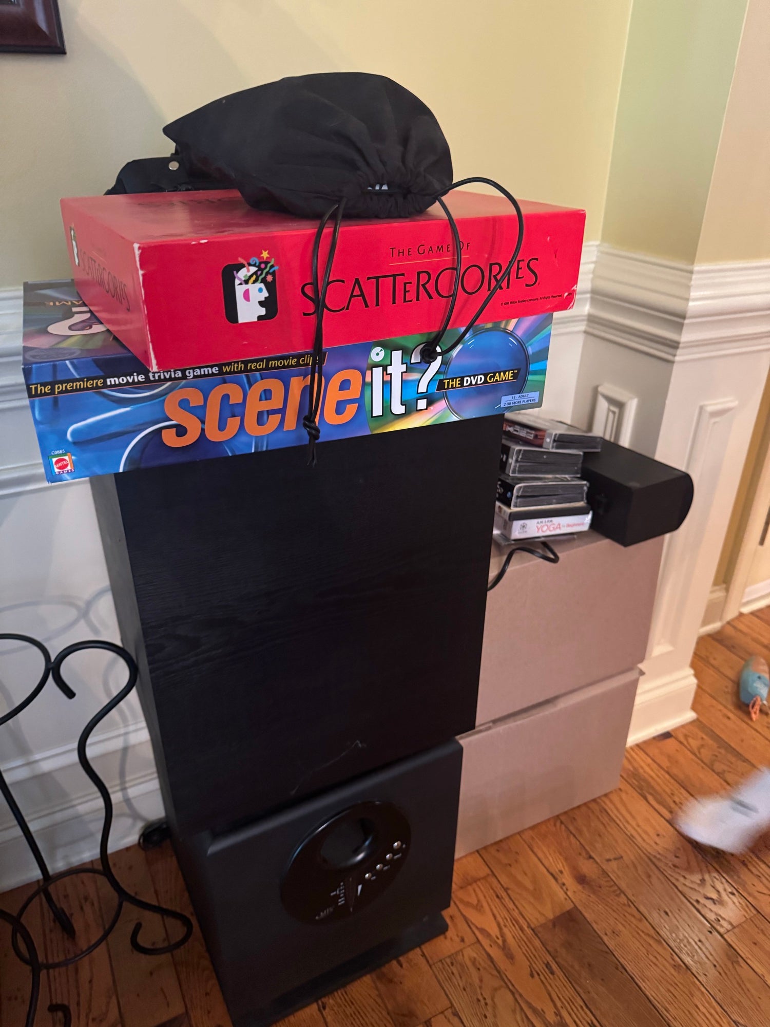 Subwoofer stacked under board games in home setting with black cloth covering top