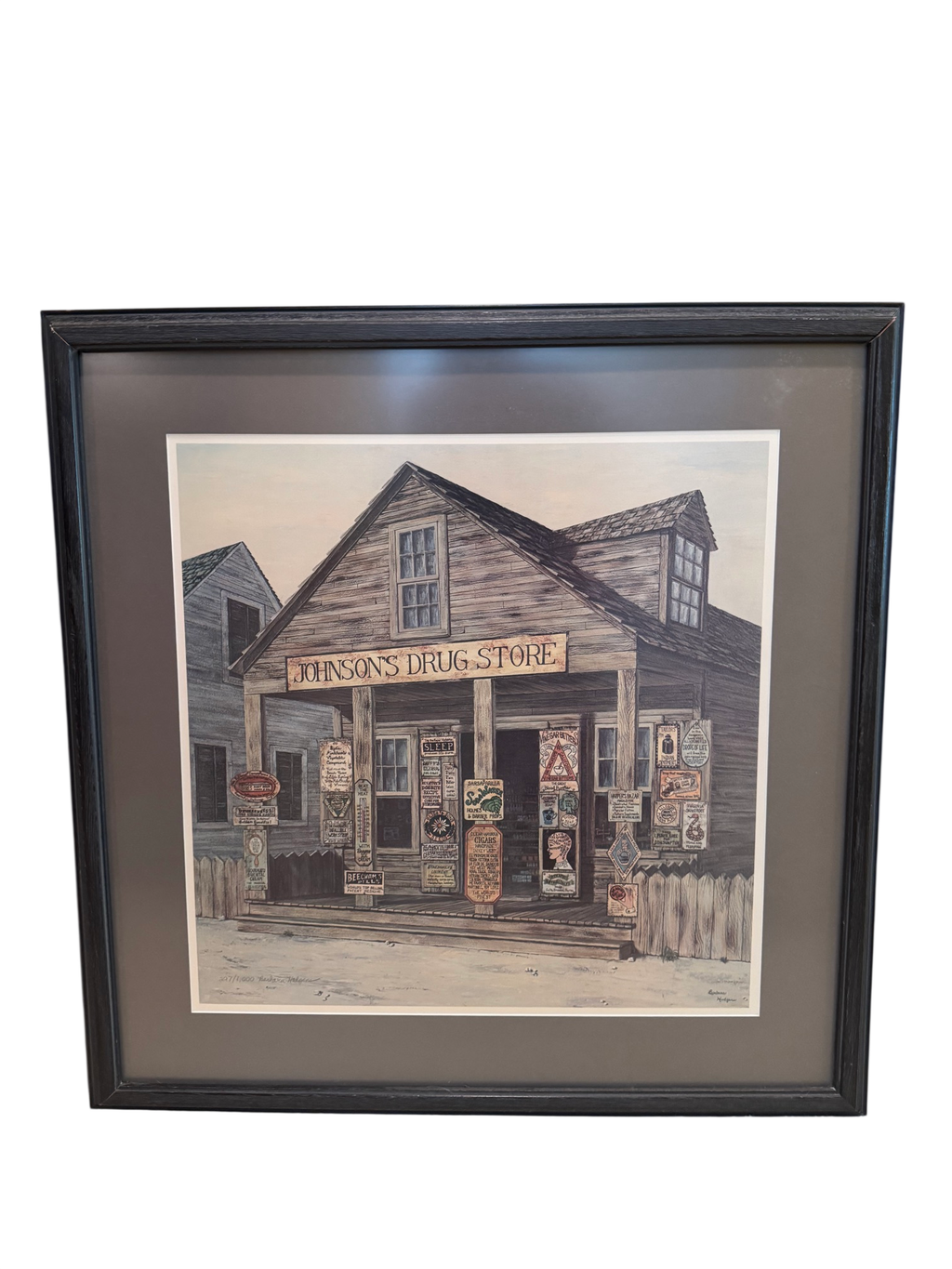Framed pen and ink watercolour print of Johnson's Drug Store, a weathered wooden country store with signage, dormers and porch, signed by Barbara Hodgeman