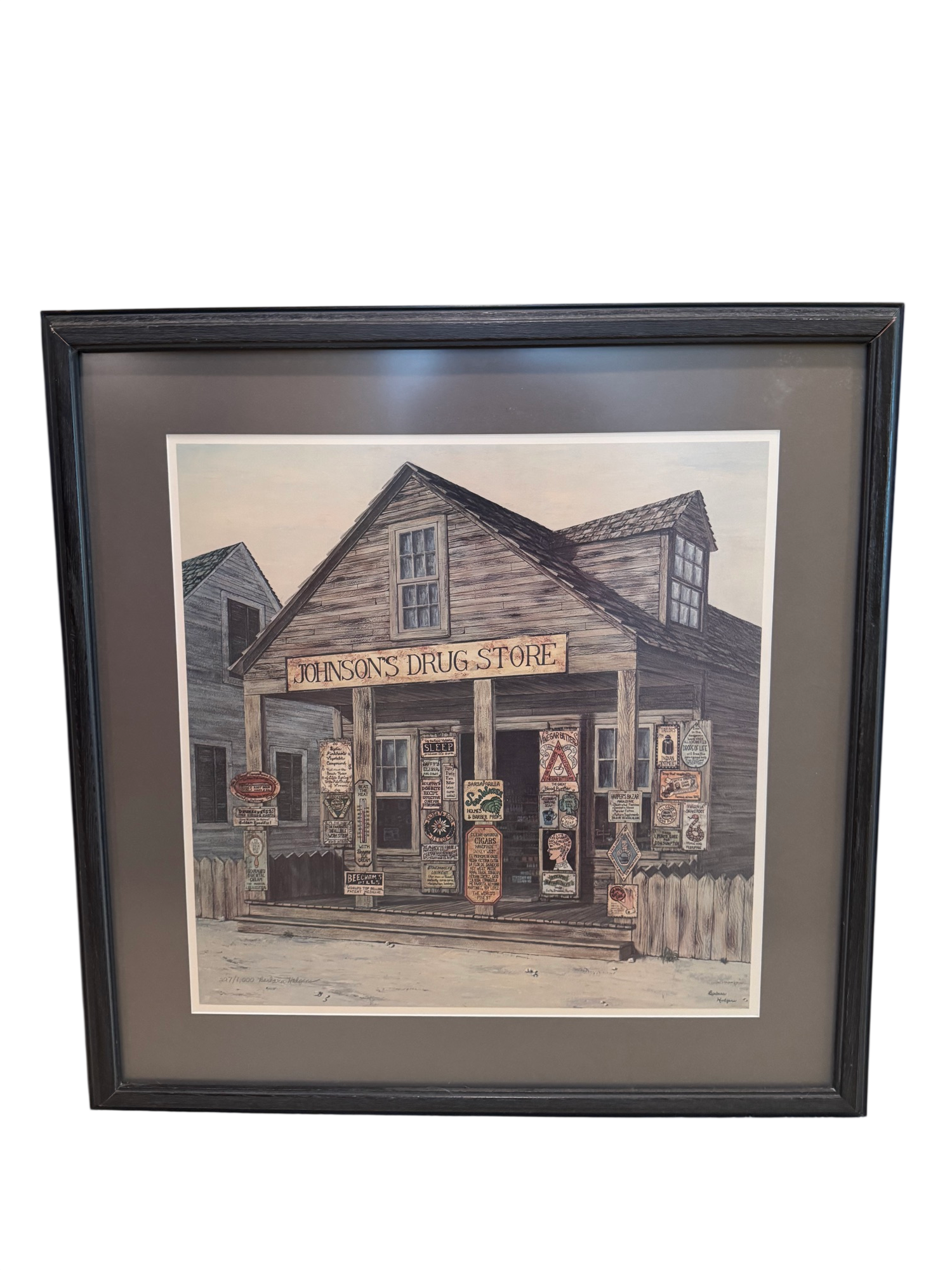 Framed pen and ink watercolour print of Johnson's Drug Store, a weathered wooden country store with signage, dormers and porch, signed by Barbara Hodgeman