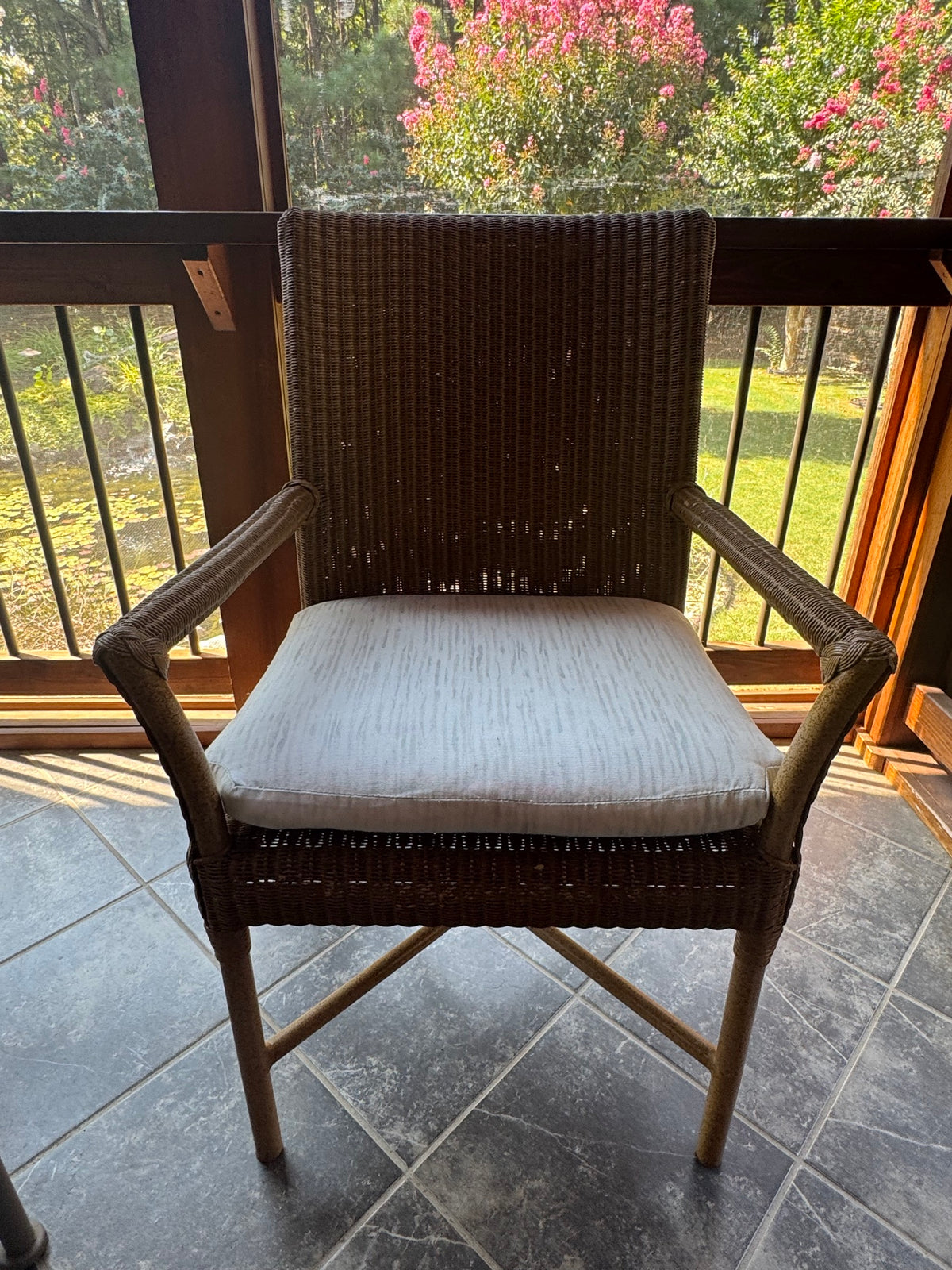 Single woven resin wicker armchair with light gray cushion seat, dark frame, displayed against bright windows