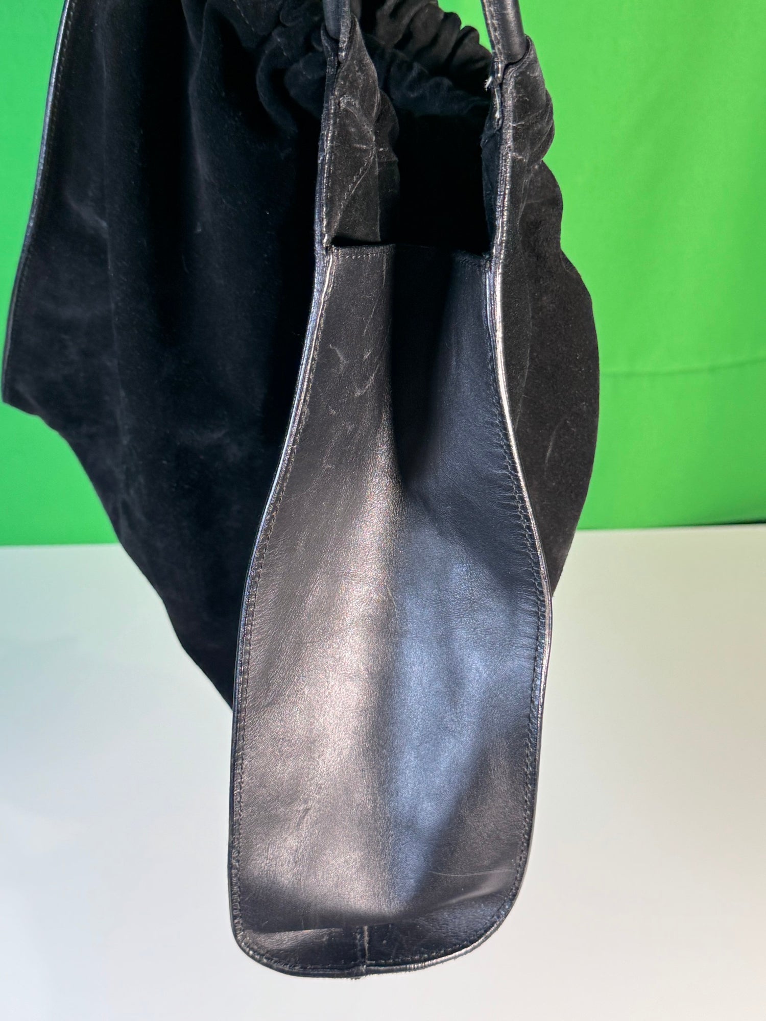 Structured leather pocket or gusset detail with seamed construction, green background