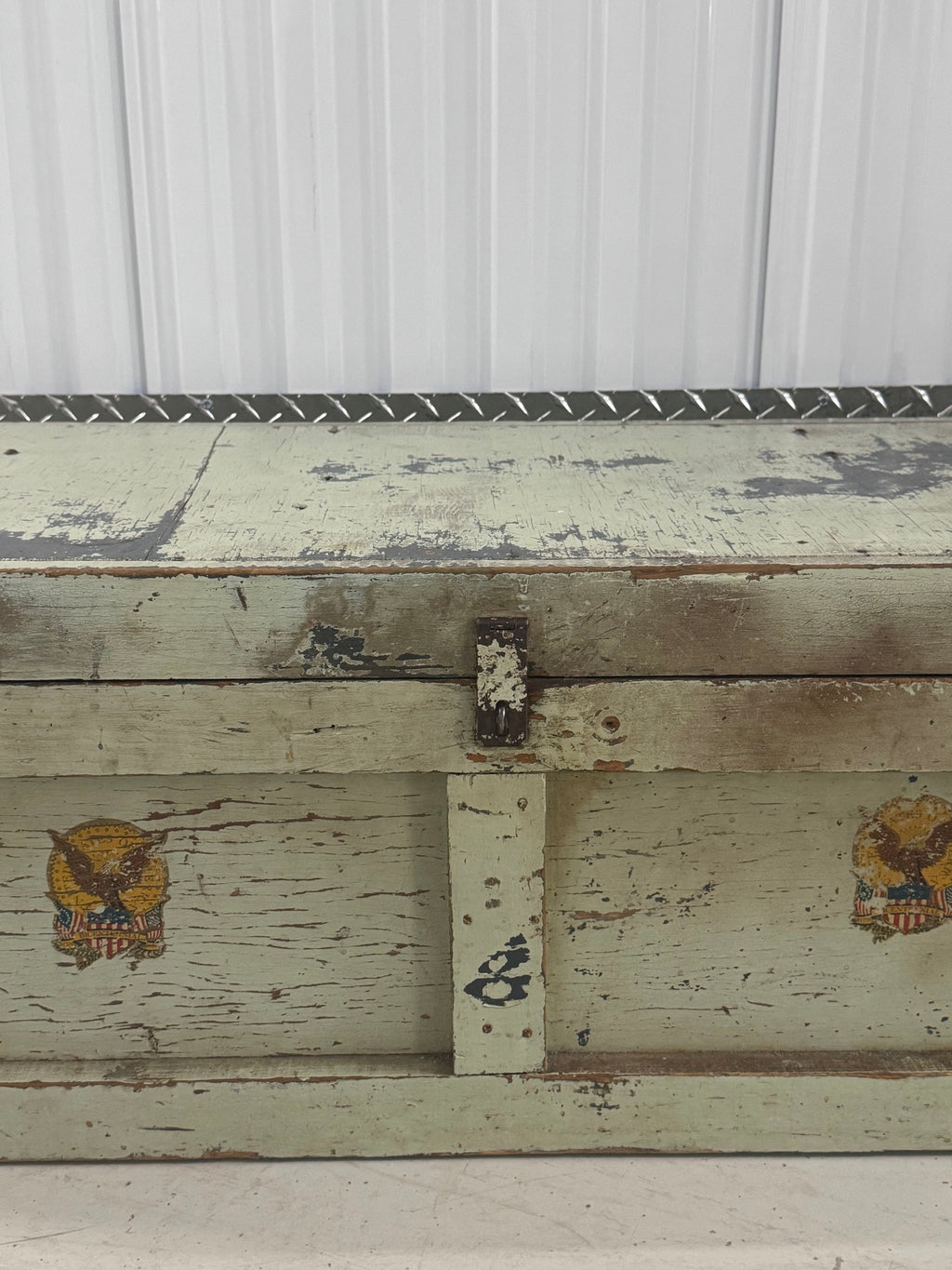 Close-up of front panel detail showing two gold eagle emblems with shield design on cream painted wood with peeling paint
