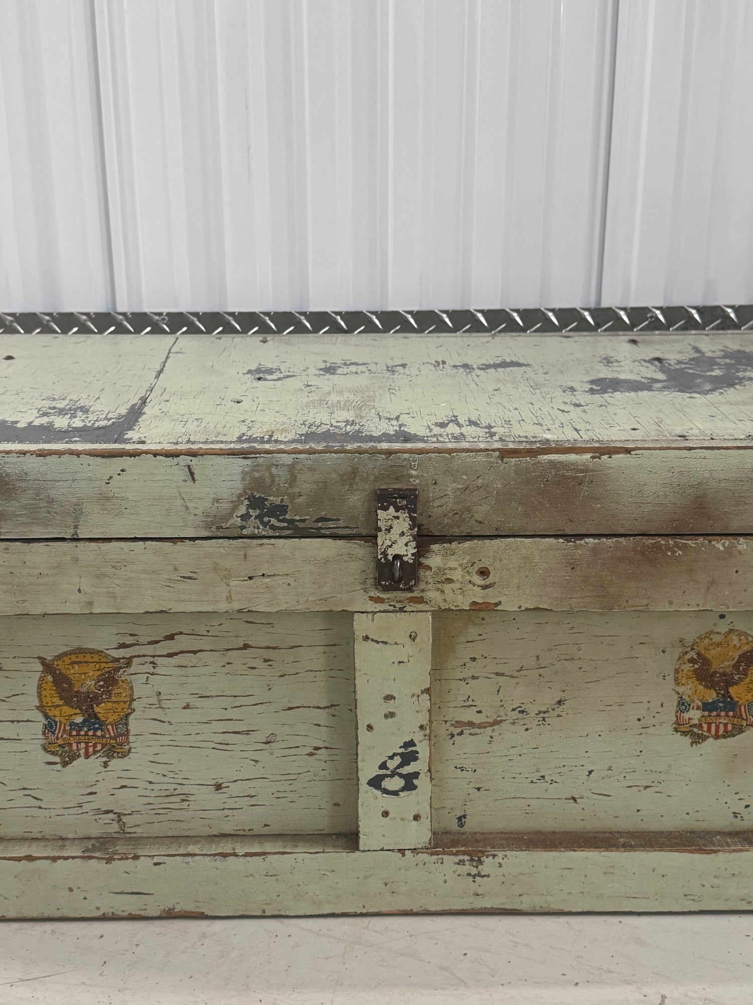 Close-up of front panel detail showing two gold eagle emblems with shield design on cream painted wood with peeling paint