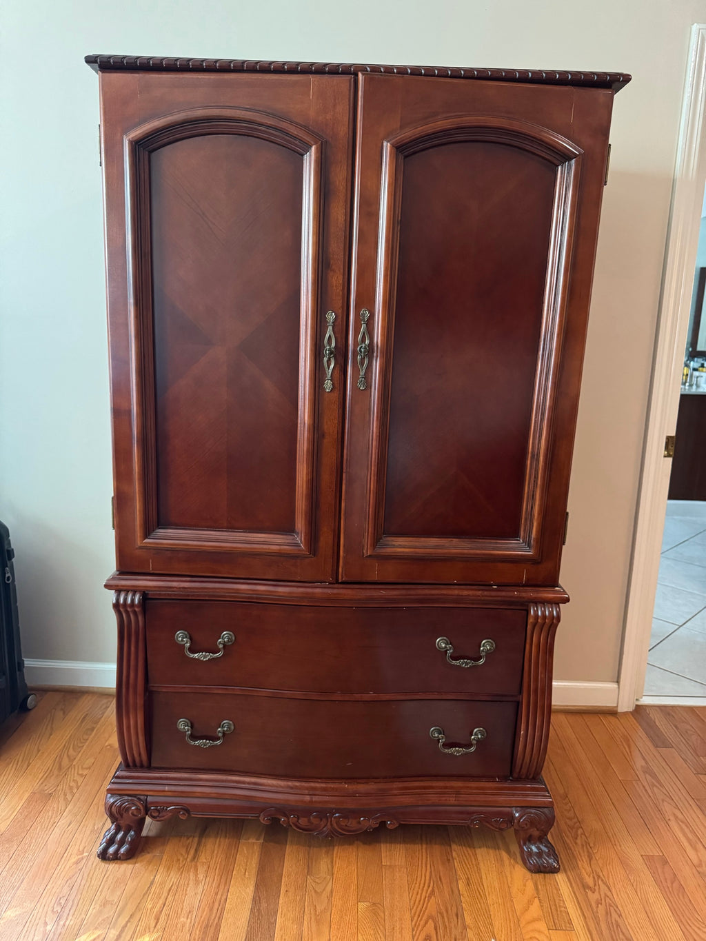 Cherry finish wood armoire with two paneled doors and two drawers on claw feet