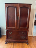 Cherry finish wood armoire with two paneled doors and two drawers on claw feet