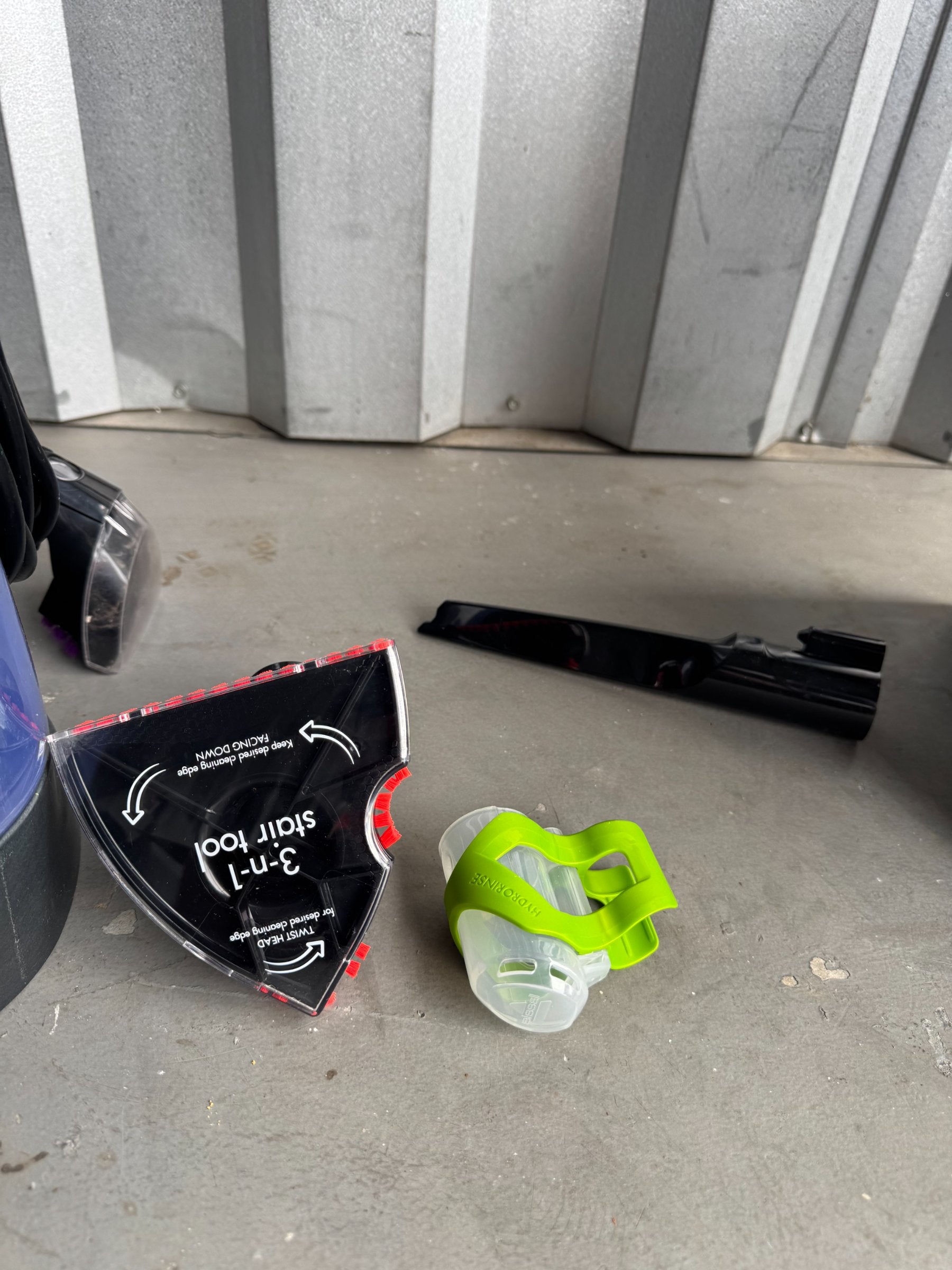 Accessories laid out on concrete floor including stain tool package, black attachment pieces, and green cleaning brush